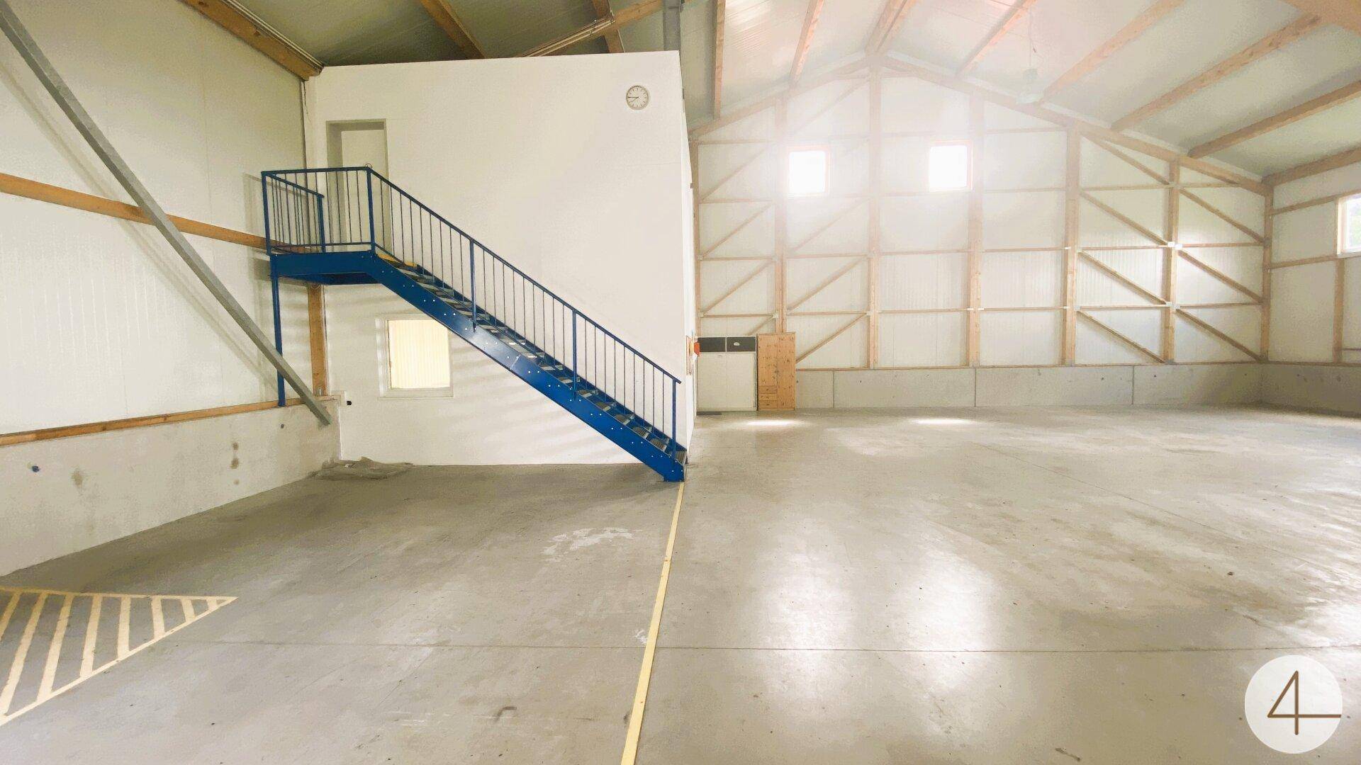Helle Lagerhalle mit Betonboden, blauer Stahltreppe und sichtbarer Holzkonstruktion.