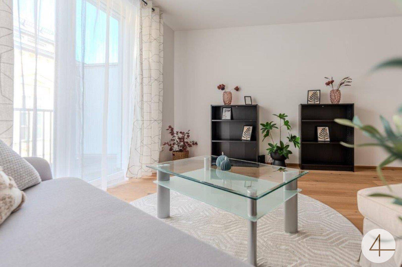 Heller Wohnbereich mit moderner Couch, Glastisch und großem Fenster zum Balkon.