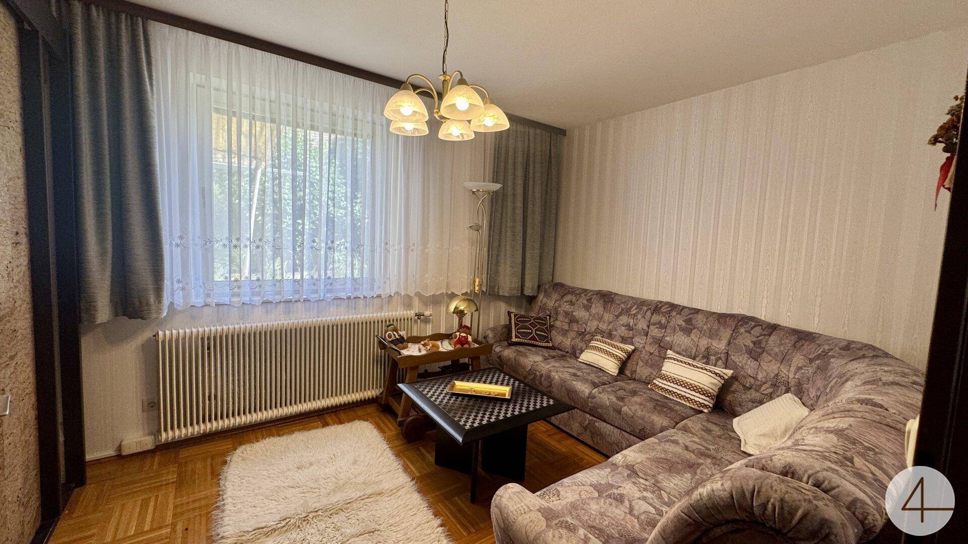 Wohnzimmer mit großem Ecksofa, Couchtisch und Parkettboden, hell durch Fenster.