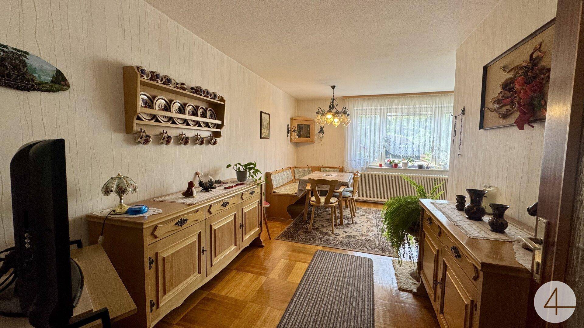 Gemütlicher Wohn-Essbereich mit traditionellen Holzmöbeln, Parkettboden und Fensterblick.