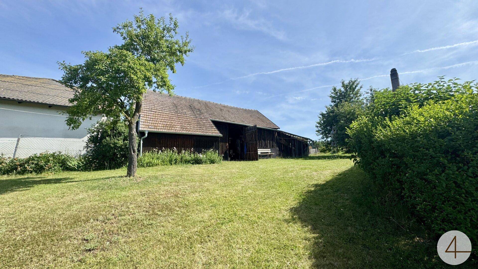 Rustikales Holzgebäude mit Ziegeldach, umgeben von einer grünen Wiese und Bäumen.