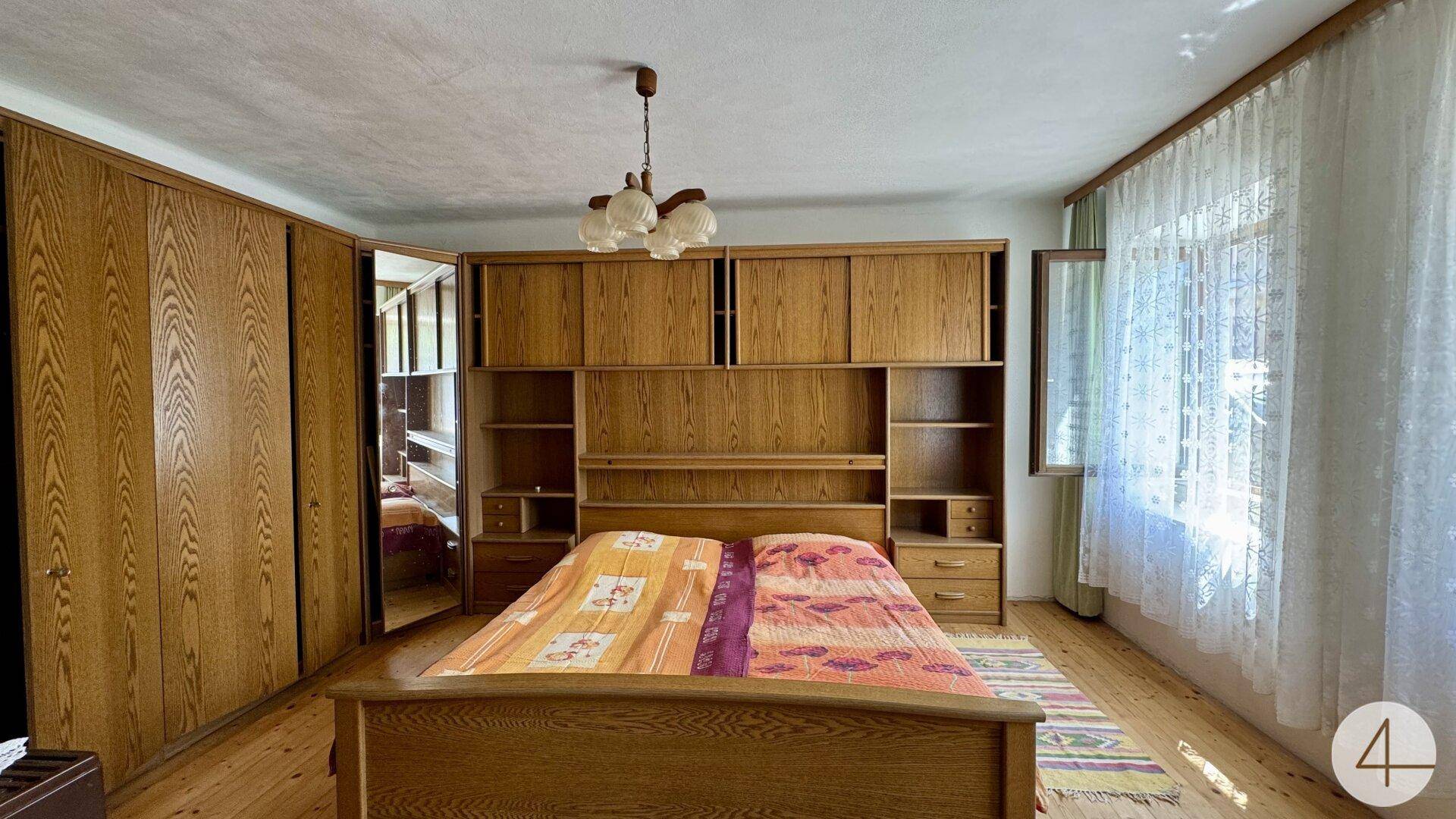 Schlafzimmer mit großem Holzbett, Einbauschränken und Fenster mit Vorhängen.