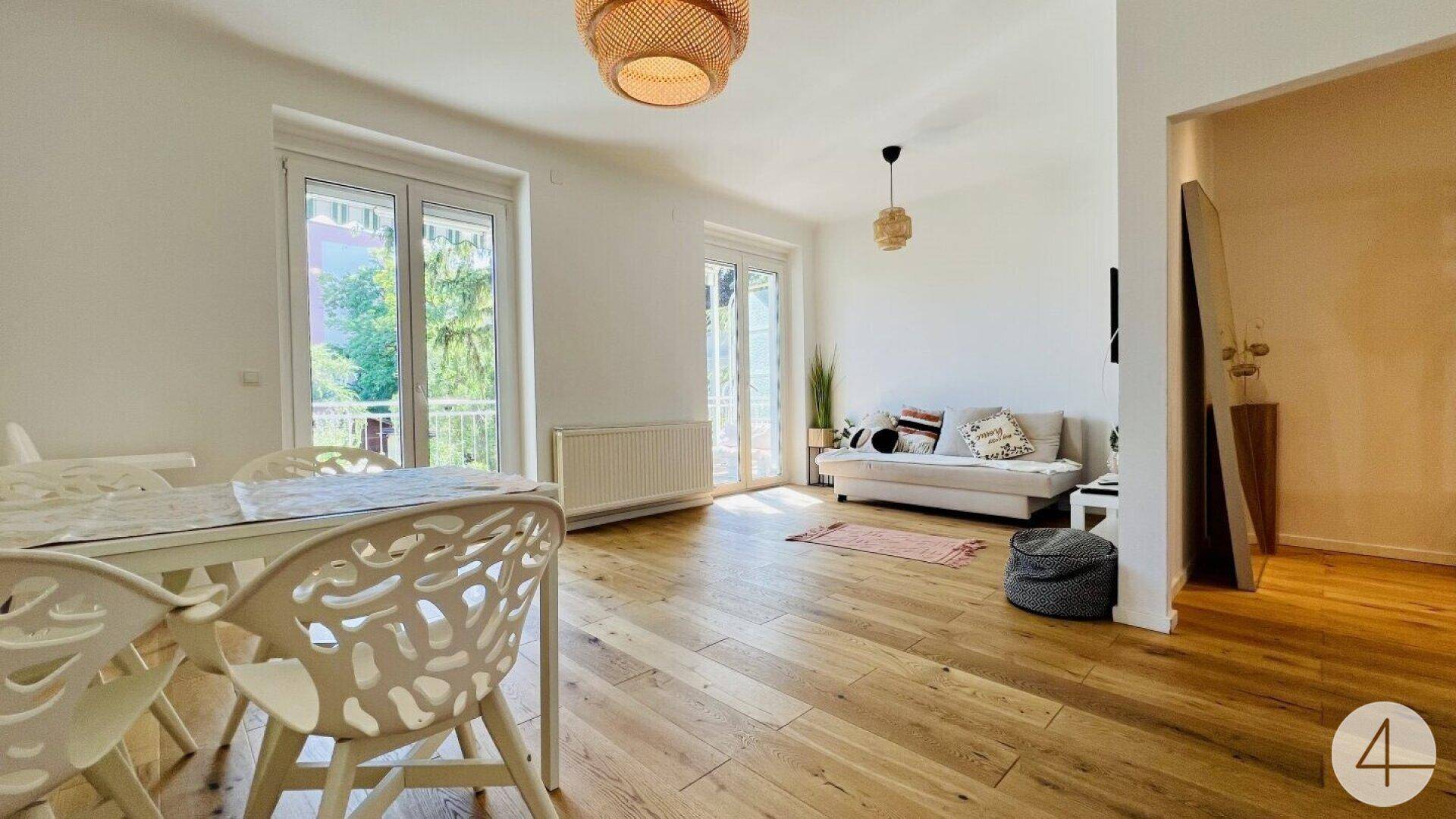 Heller Wohn-Essbereich mit Holzboden, modernen Möbeln und Zugang zum Balkon.