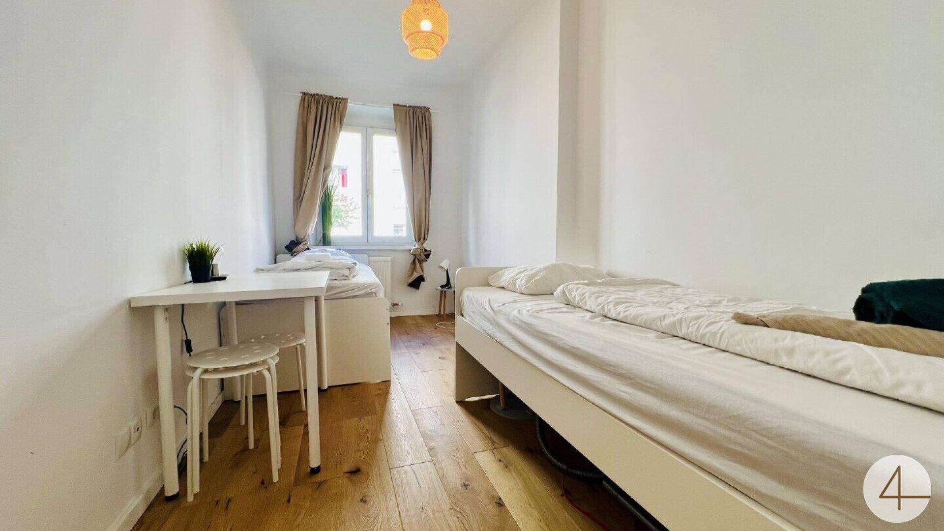 Helles Schlafzimmer mit zwei Einzelbetten, Holzboden und einem Fenster.