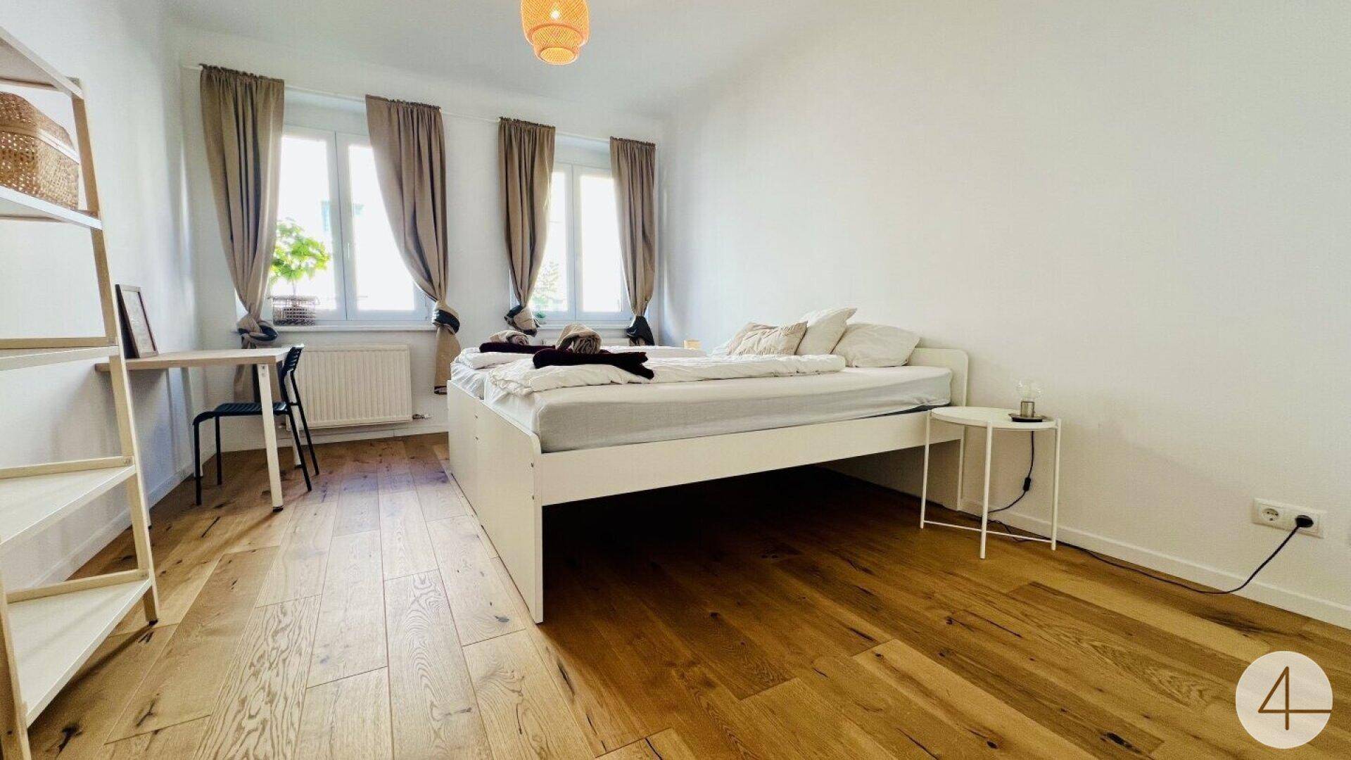 Gemütliches Schlafzimmer mit Holzboden, Doppelbett und zwei Fenstern für viel Tageslicht.