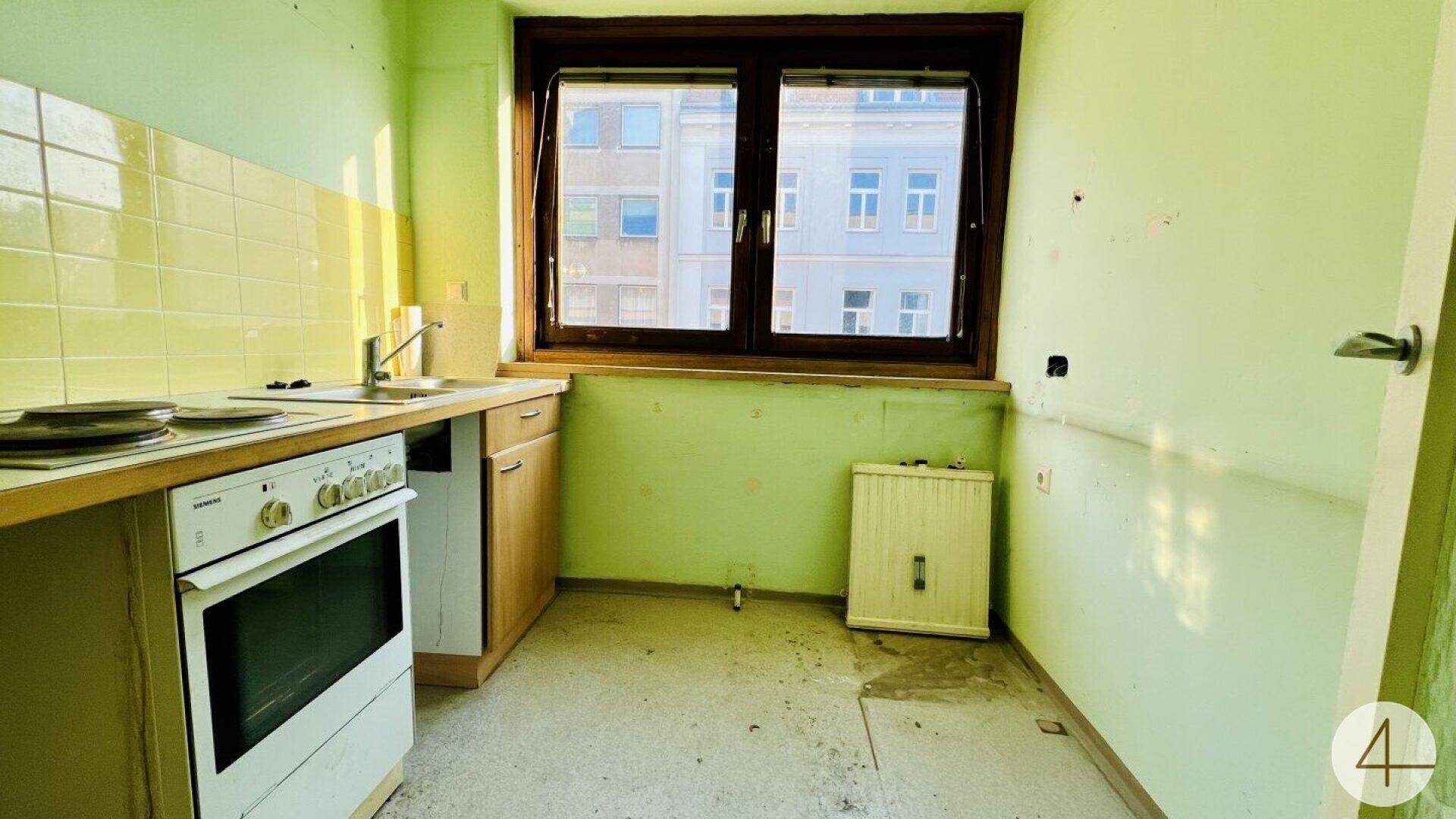 Veraltete Küche mit grünen Wänden, einfachen Fliesen und einem Fenster, das renoviert werden muss.