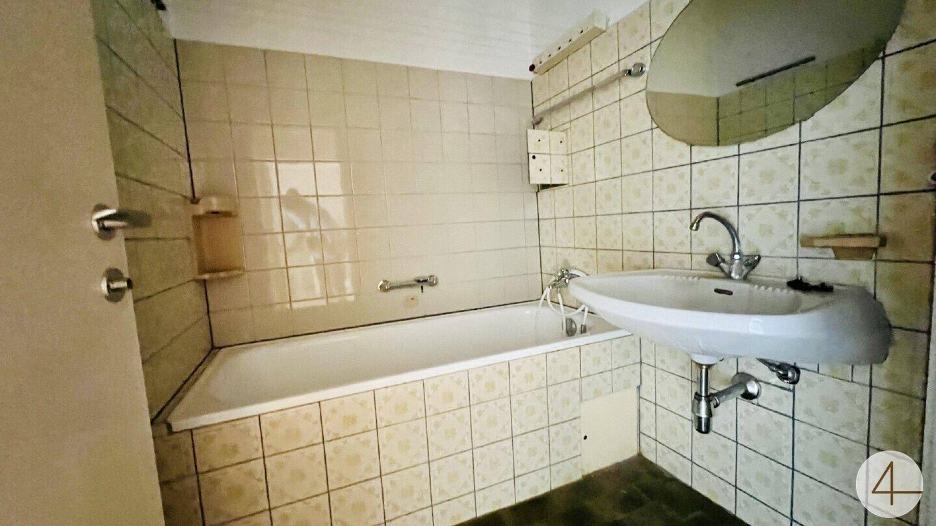 Badezimmer im 80er-Jahre-Stil mit beigen Fliesen, Badewanne und Waschbecken.