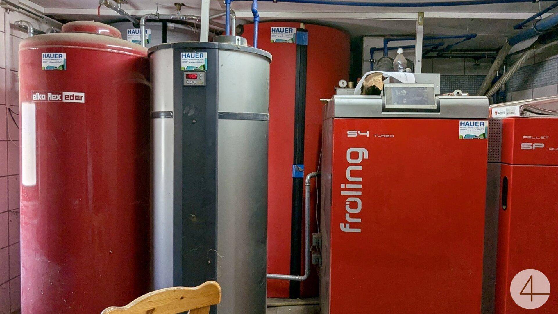 Heizungsraum mit großen roten Warmwasserspeichern und einem modernen Pelletkessel.