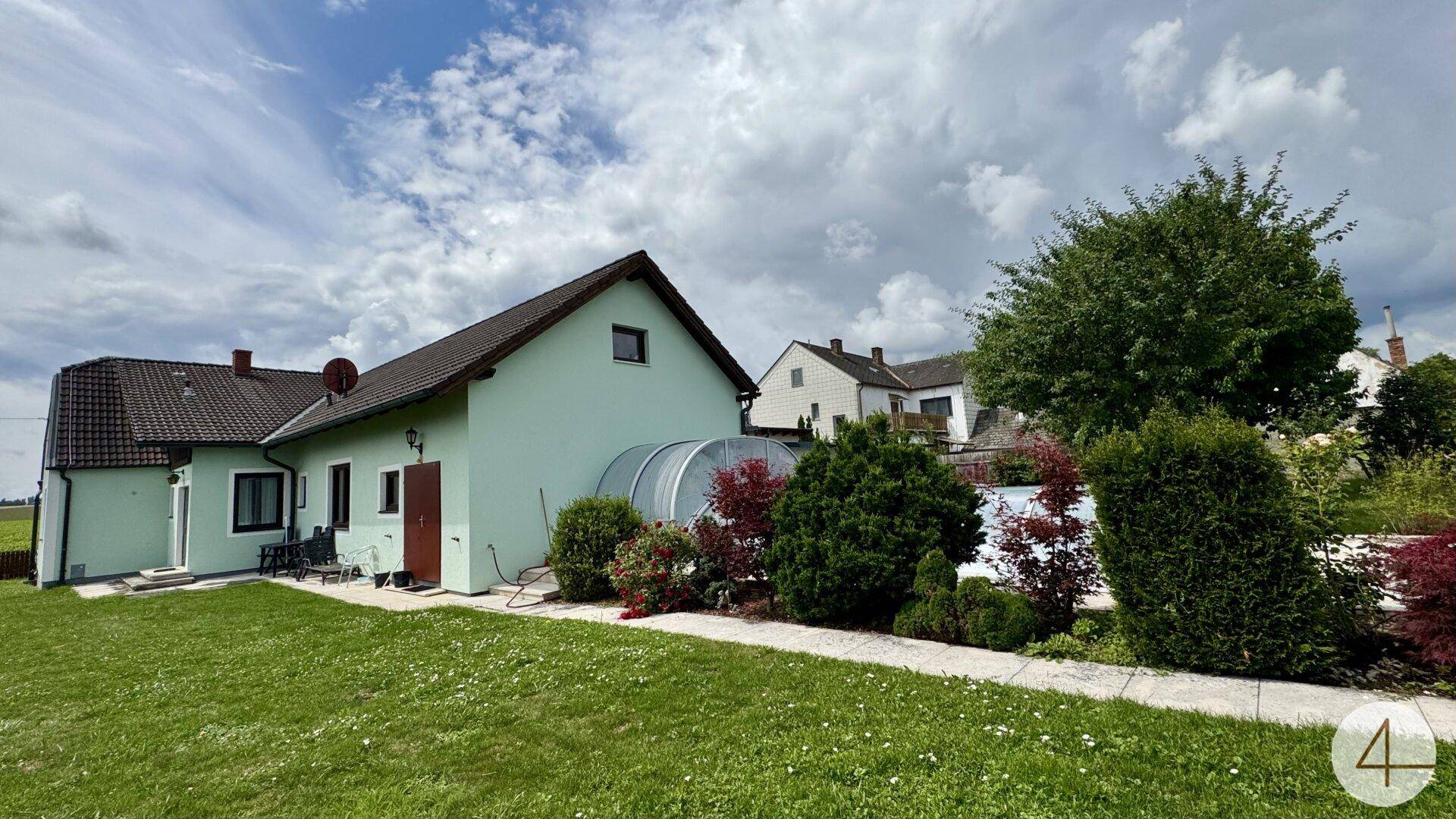 Gartenansicht des Hauses mit Rasenfläche, Terrasse und dem überdachten Poolbereich.