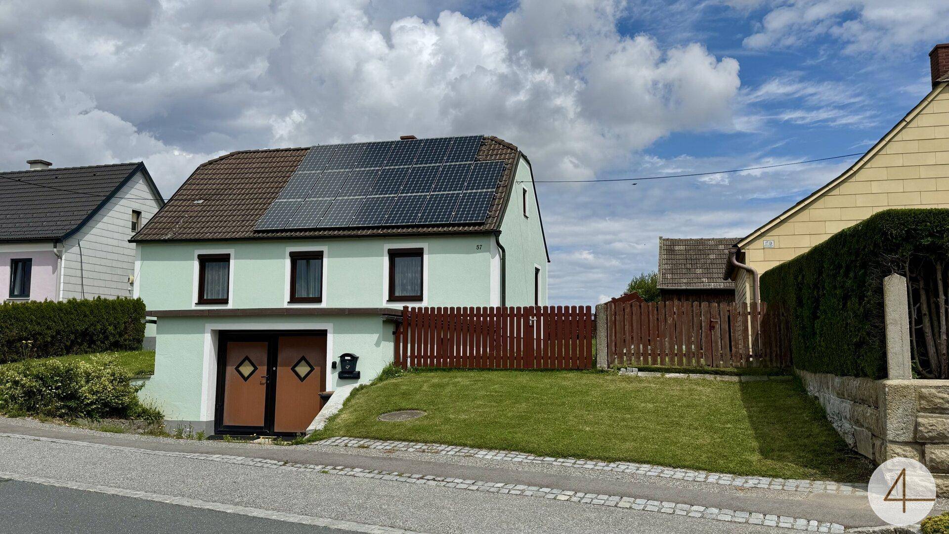 Vorderansicht des Hauses von der Straße mit Solaranlage auf dem Dach und Garageneinfahrt.