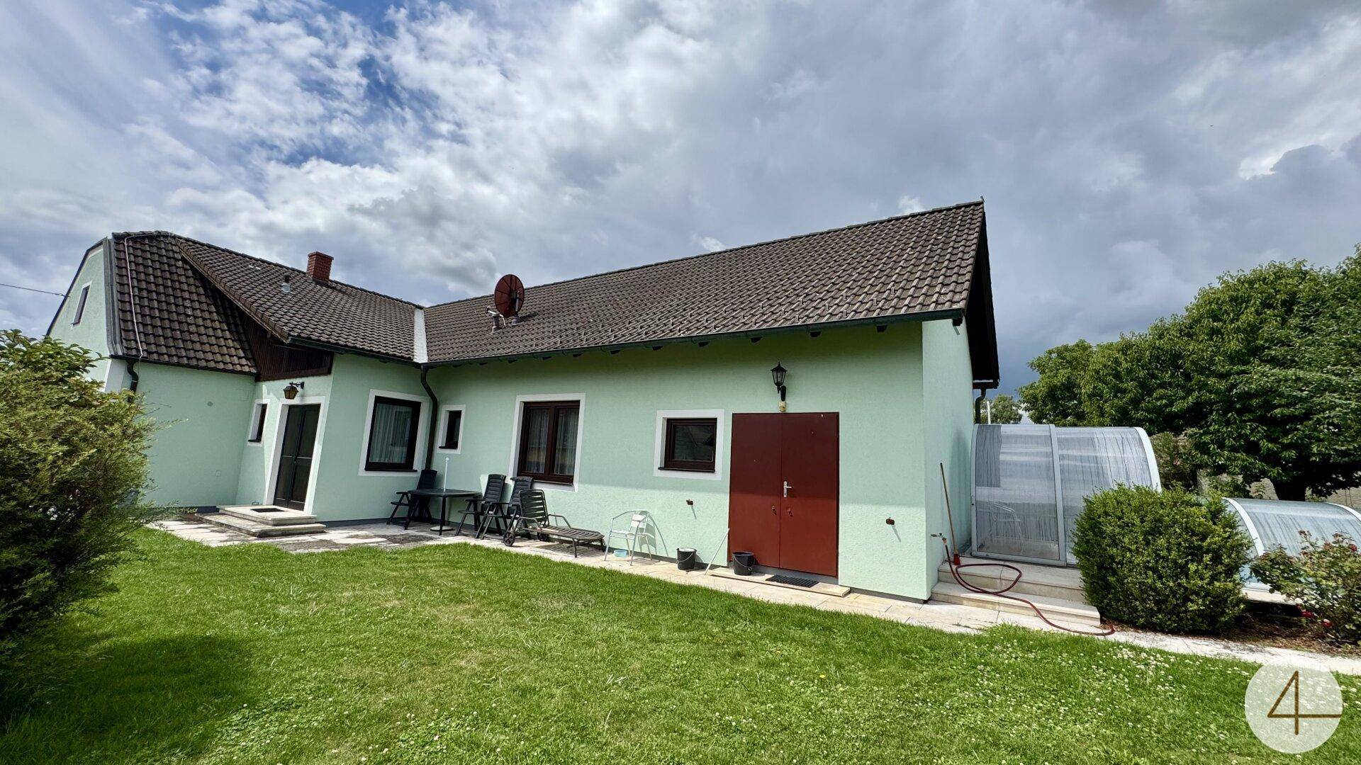 Weitläufiger Gartenbereich des Hauses mit Rasen, Terrasse und dem überdachten Pool im Hintergrund.