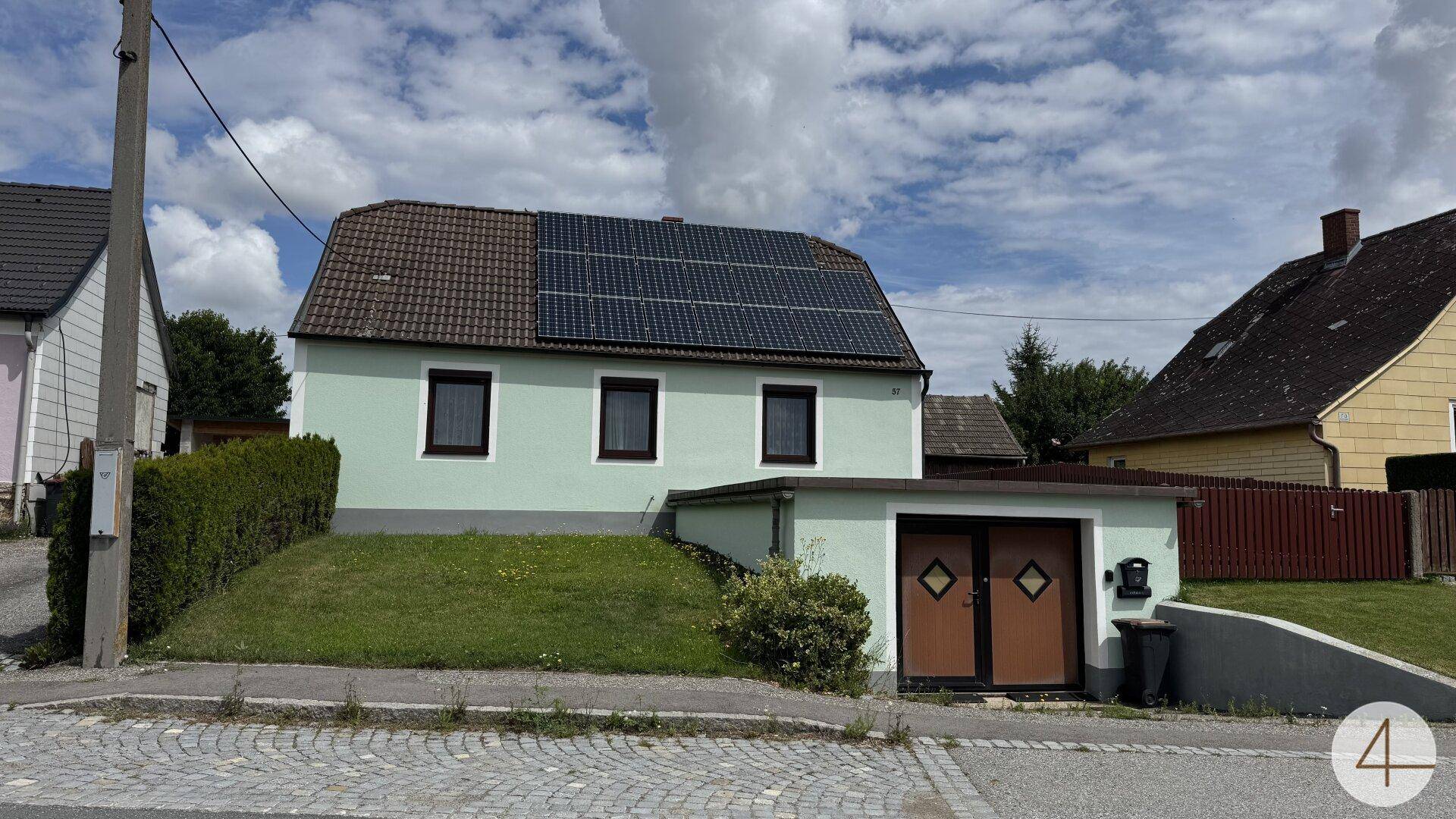 Ansicht des Hauses von der Straße mit Solarmodulen auf dem Dach und einer Garage im Untergeschoss.