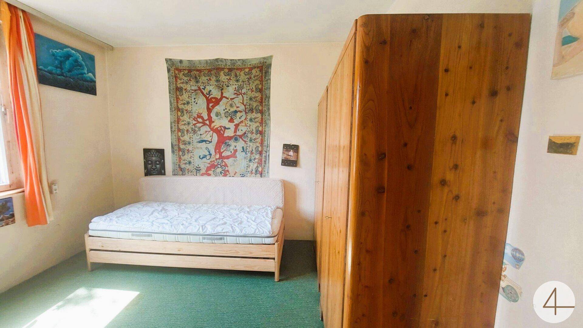 Schlafzimmer mit Bett, großem Holzschrank und grünem Teppichboden, gemütlich eingerichtet.