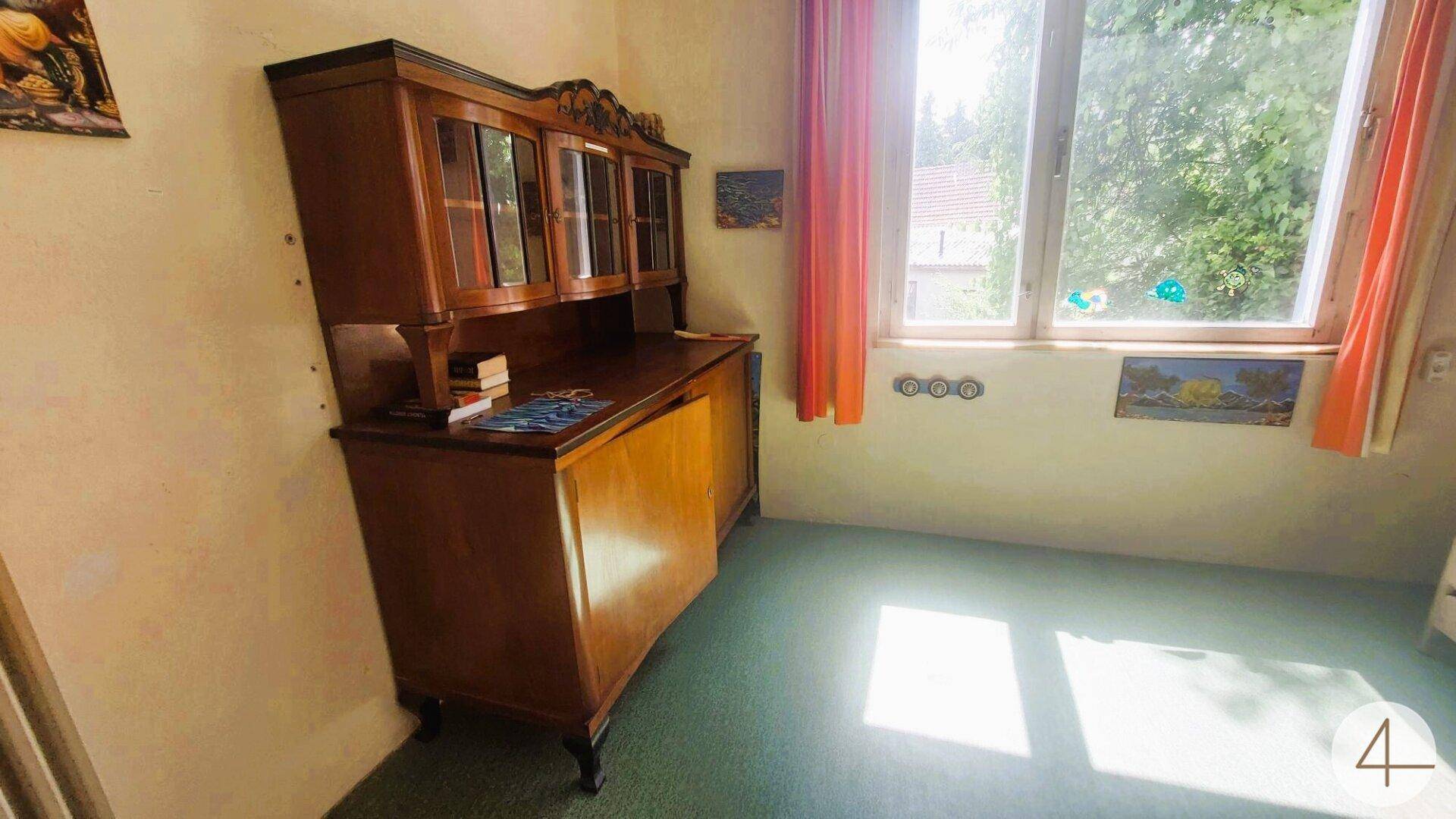 Zimmer mit antikem Holzschrank, grünem Teppichboden und großem Fenster, hell und traditionell.