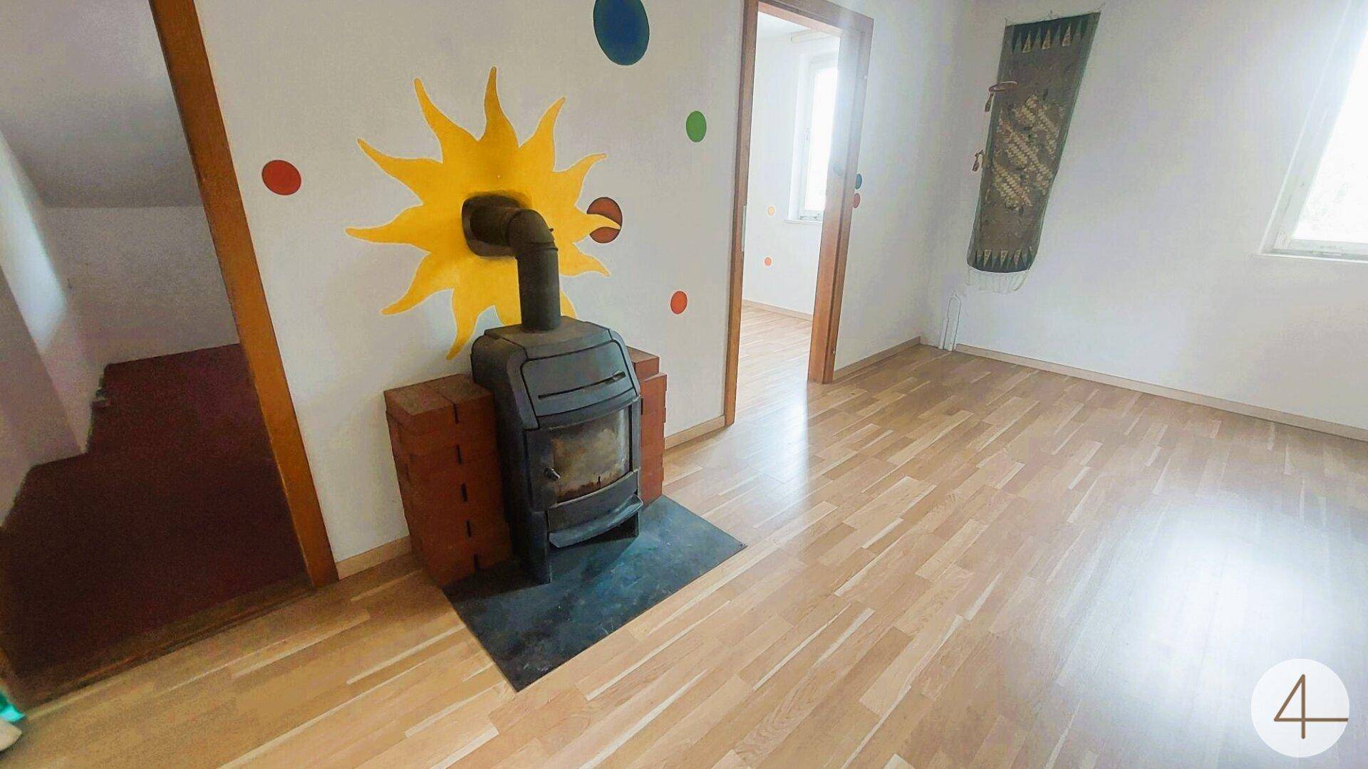 Wohnraum mit Kaminofen, Holzboden und sonniger Atmosphäre, ideal für gemütliche Stunden.