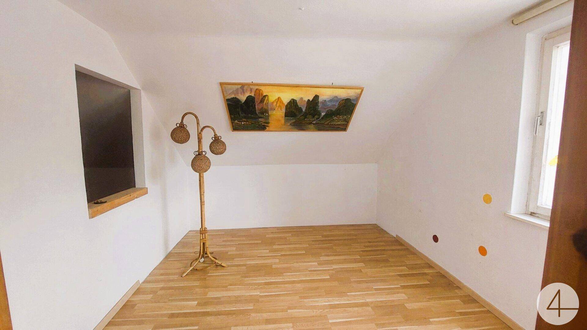 Helles Dachzimmer mit Holzboden, schrägen Wänden und einem Fenster für natürliches Licht.