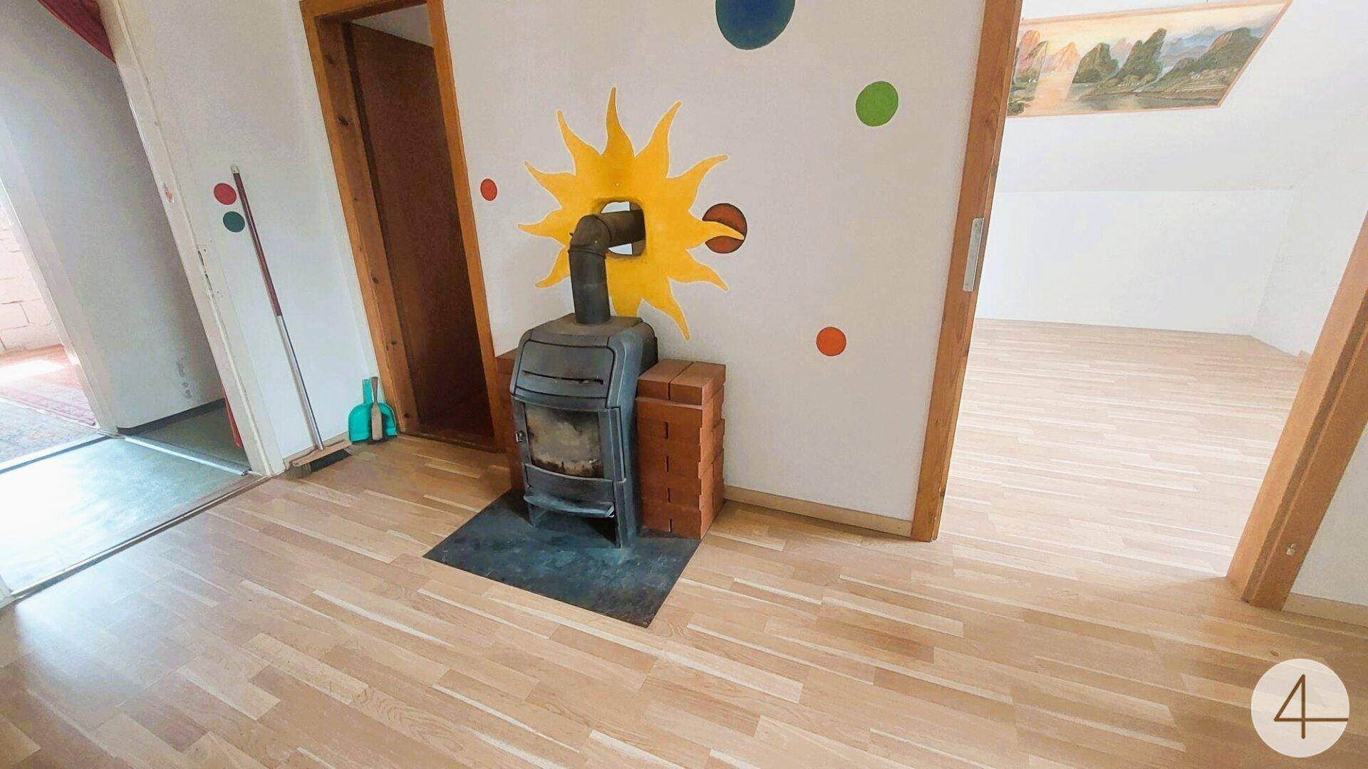Gemütlicher Raum mit Holzboden, einem Kaminofen und farbenfroher Wanddekoration.
