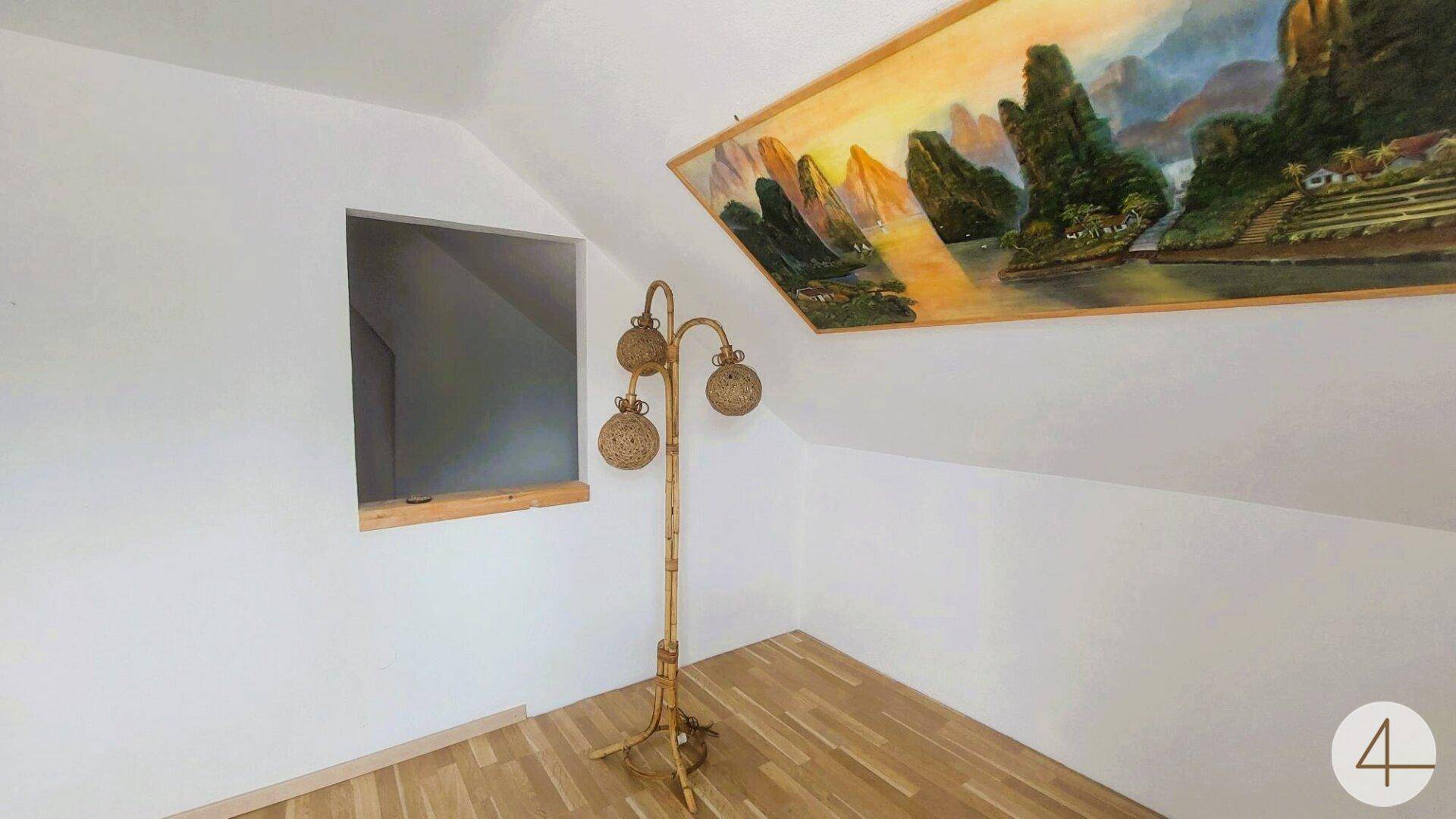 Dachzimmer mit schrägen Wänden, Holzboden und einem dekorativen Gemälde an der Wand.