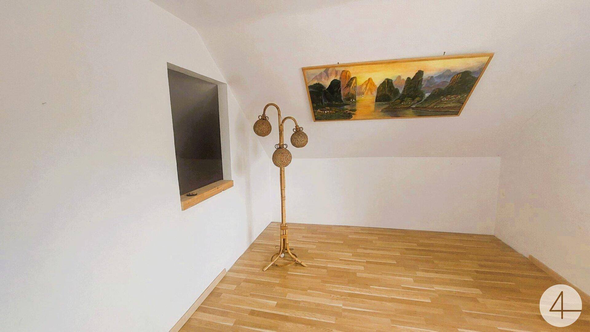 Dachzimmer mit Holzboden, schrägen Wänden und einem Fenster, das viel Licht hereinlässt.