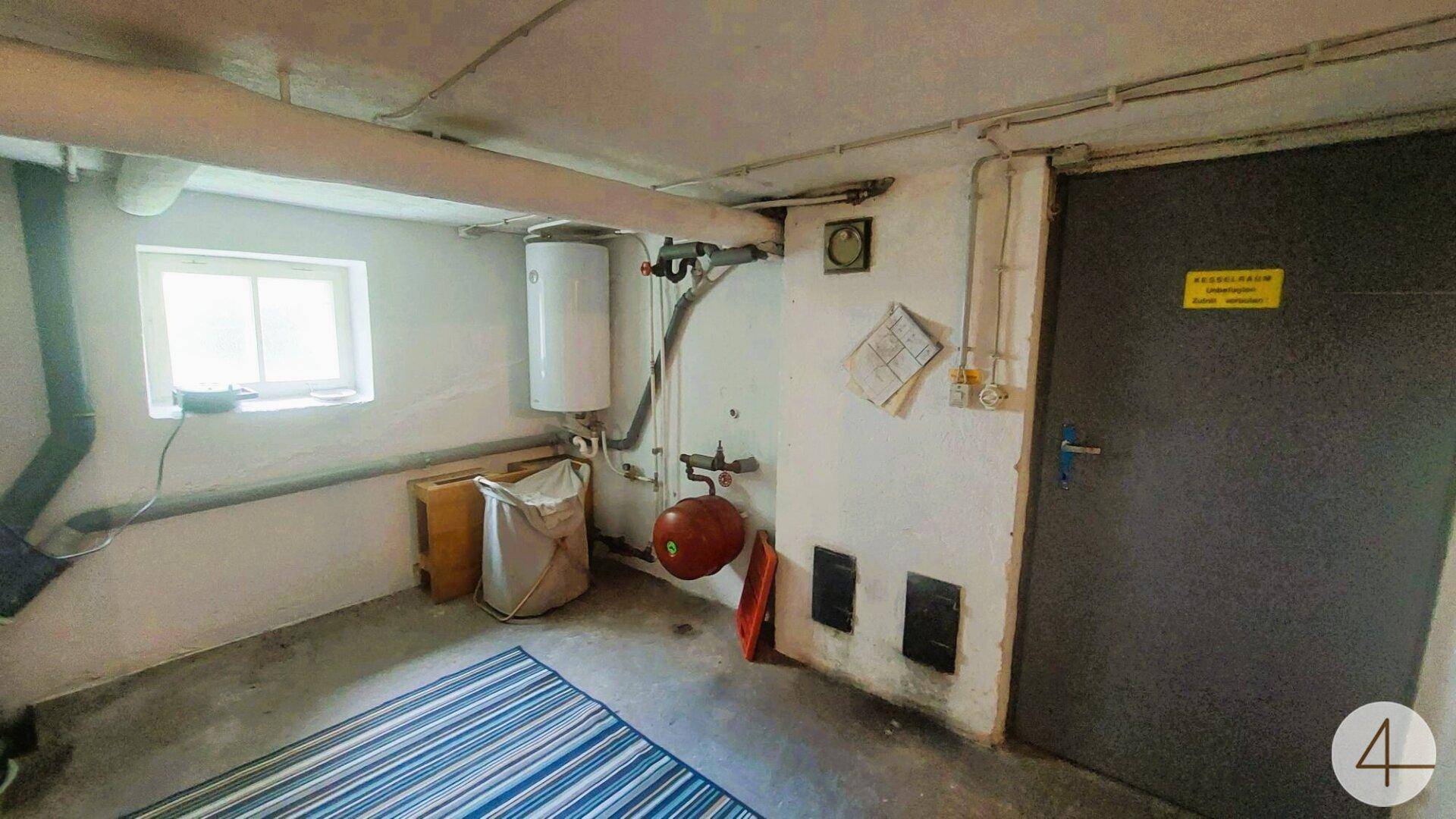 Hauswirtschaftsraum im Keller mit Warmwasserbereiter, Leitungen und einem Fenster.