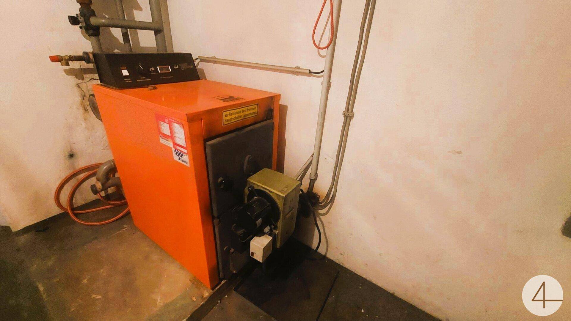 Heizungsraum im Keller mit einem orangefarbenen Heizkessel und Rohrleitungen.