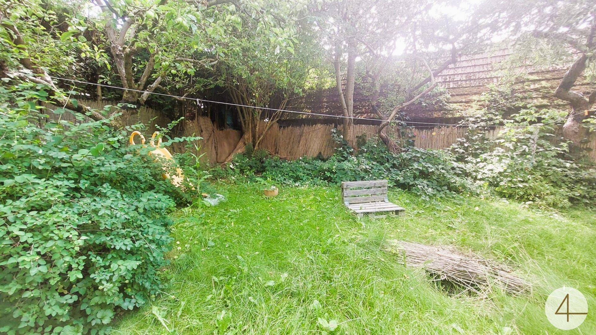 Großer, naturbelassener Gartenbereich mit Rasenfläche, Bäumen und einer kleinen Sitzbank.