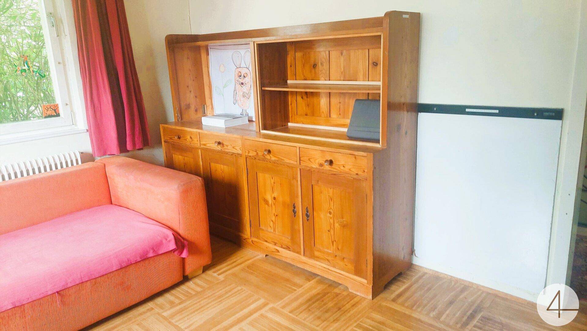 Wohnraum mit Holzschrank, orangefarbenem Sofa und hellem Holzboden, freundlich gestaltet.