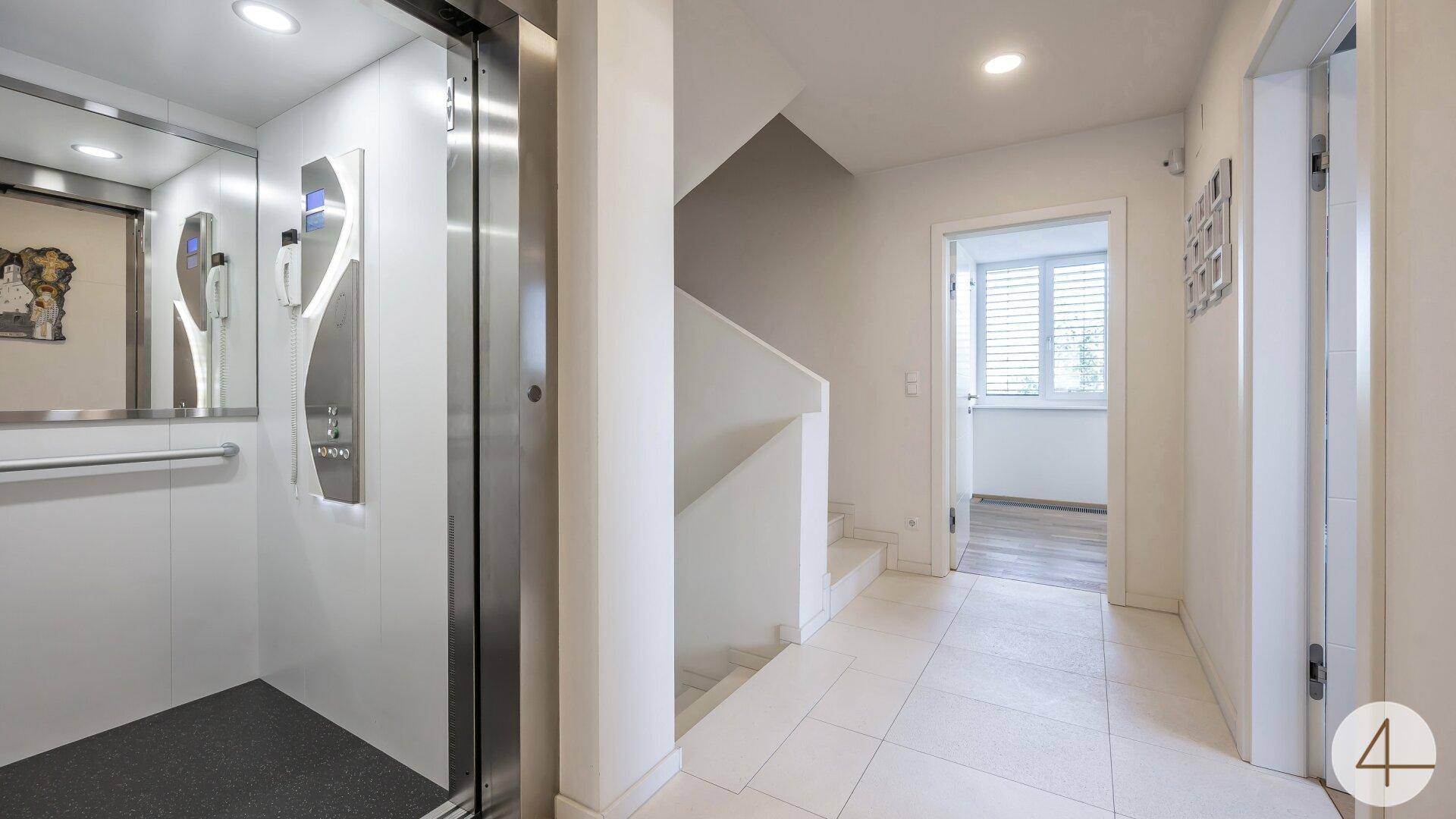 Heller Flur mit modernem Aufzug und einer eleganten Treppe, die die verschiedenen Etagen verbindet.
