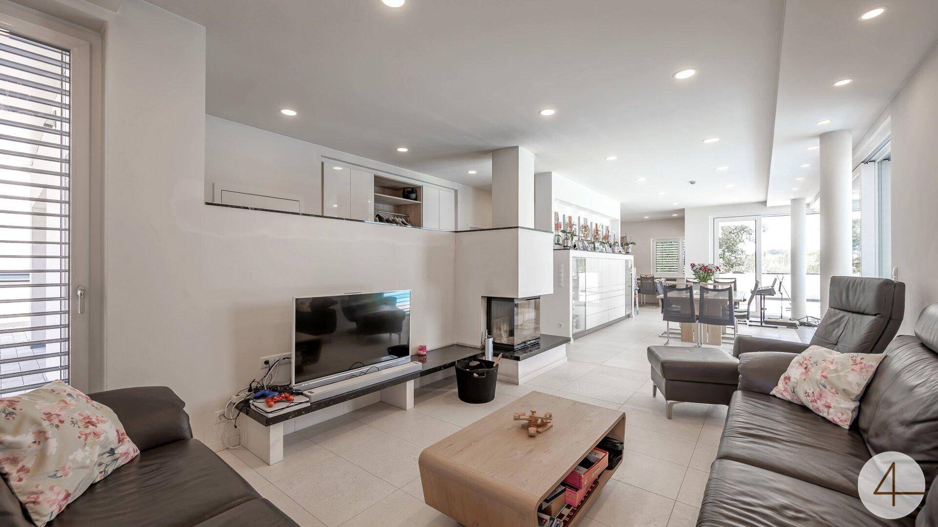 Helles Wohnzimmer mit modernem Kamin, bequemen Sofas und offenem Übergang zum Essbereich.
