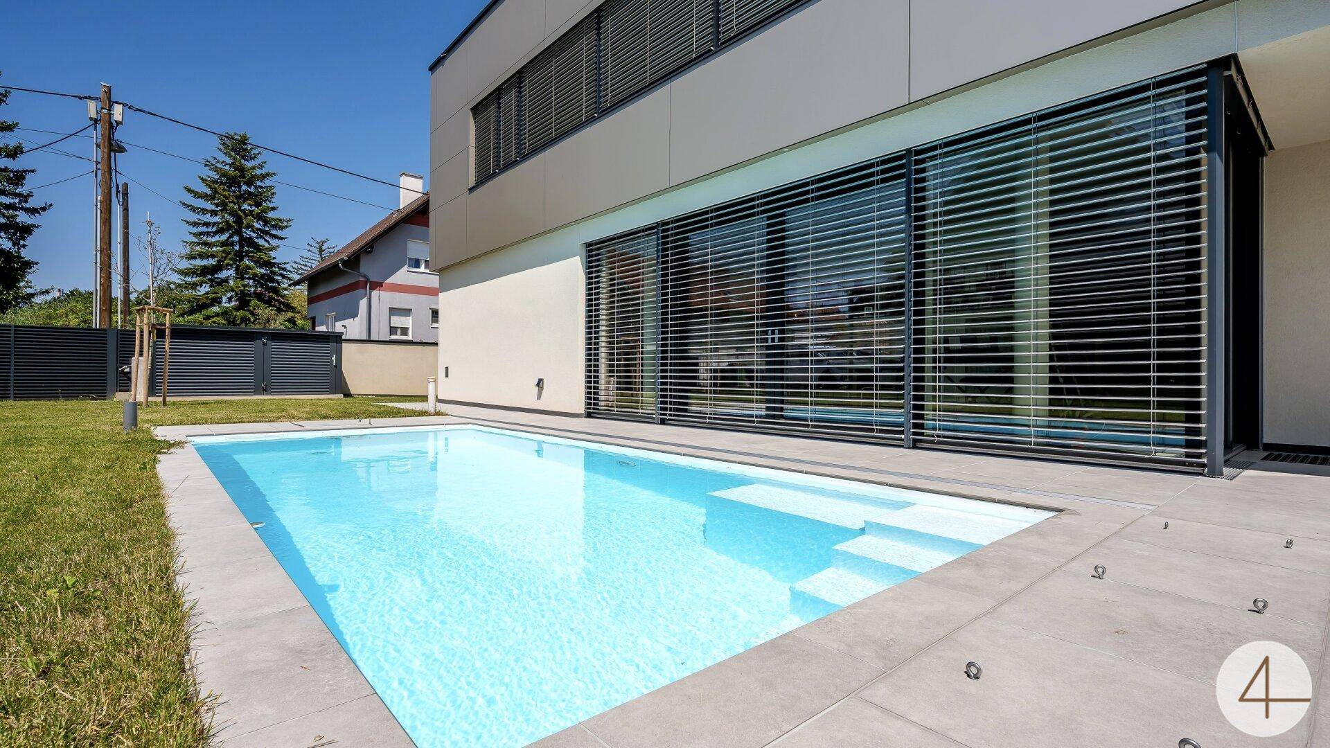 Klarer Swimmingpool mit breiten Stufen neben der modernen Hausfassade mit großen Fensterfronten.