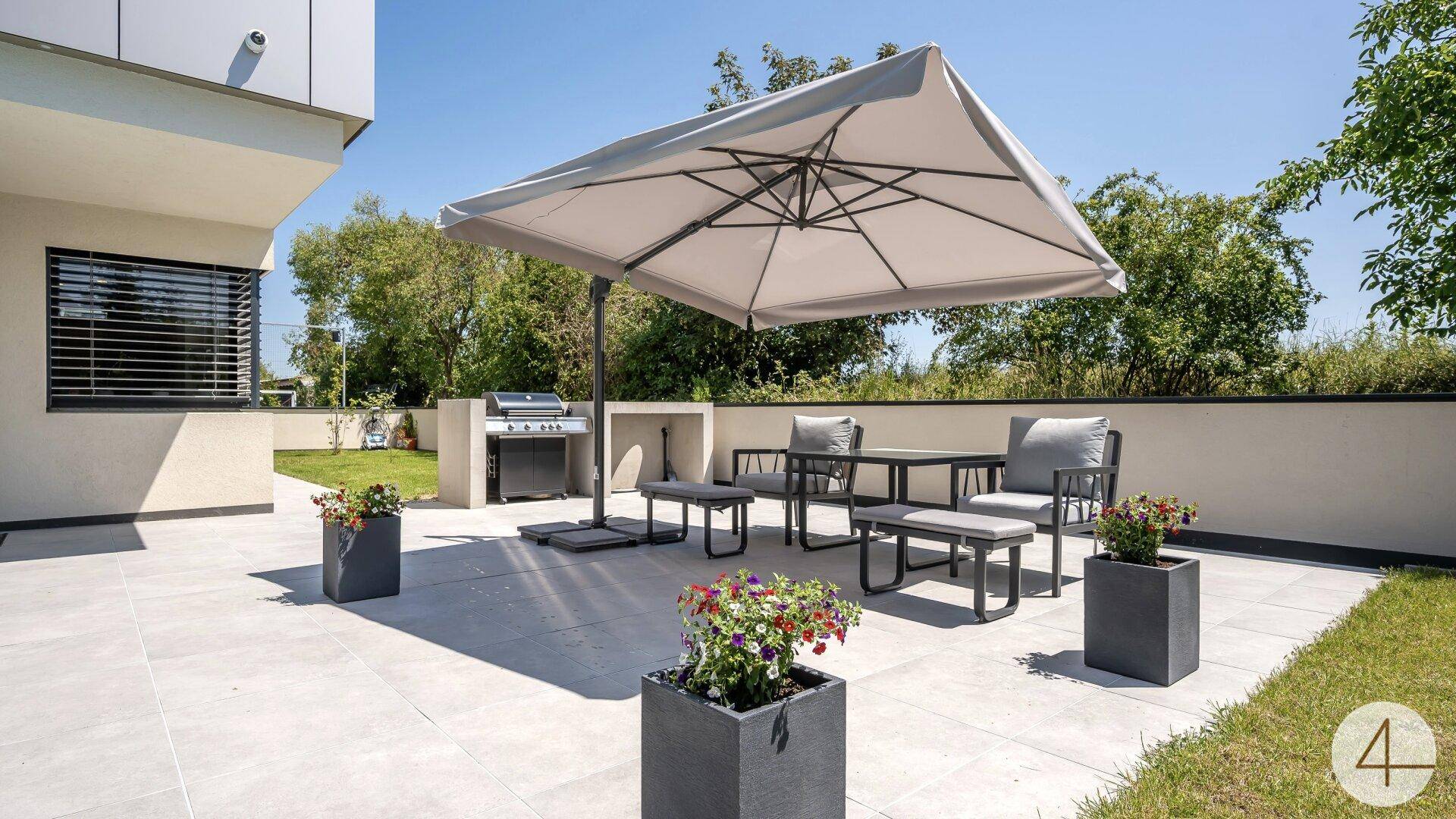 Geräumige Terrasse mit großem Sonnenschirm, Esstisch und Grillbereich, ideal für Mahlzeiten im Freien.