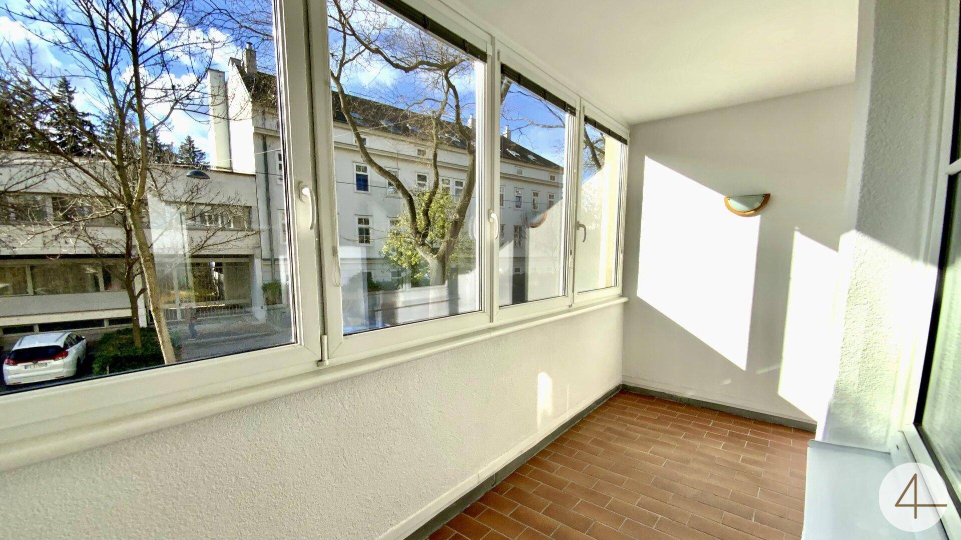 Heller, verglaster Balkon mit Fliesenboden und Blick auf den Innenhof.