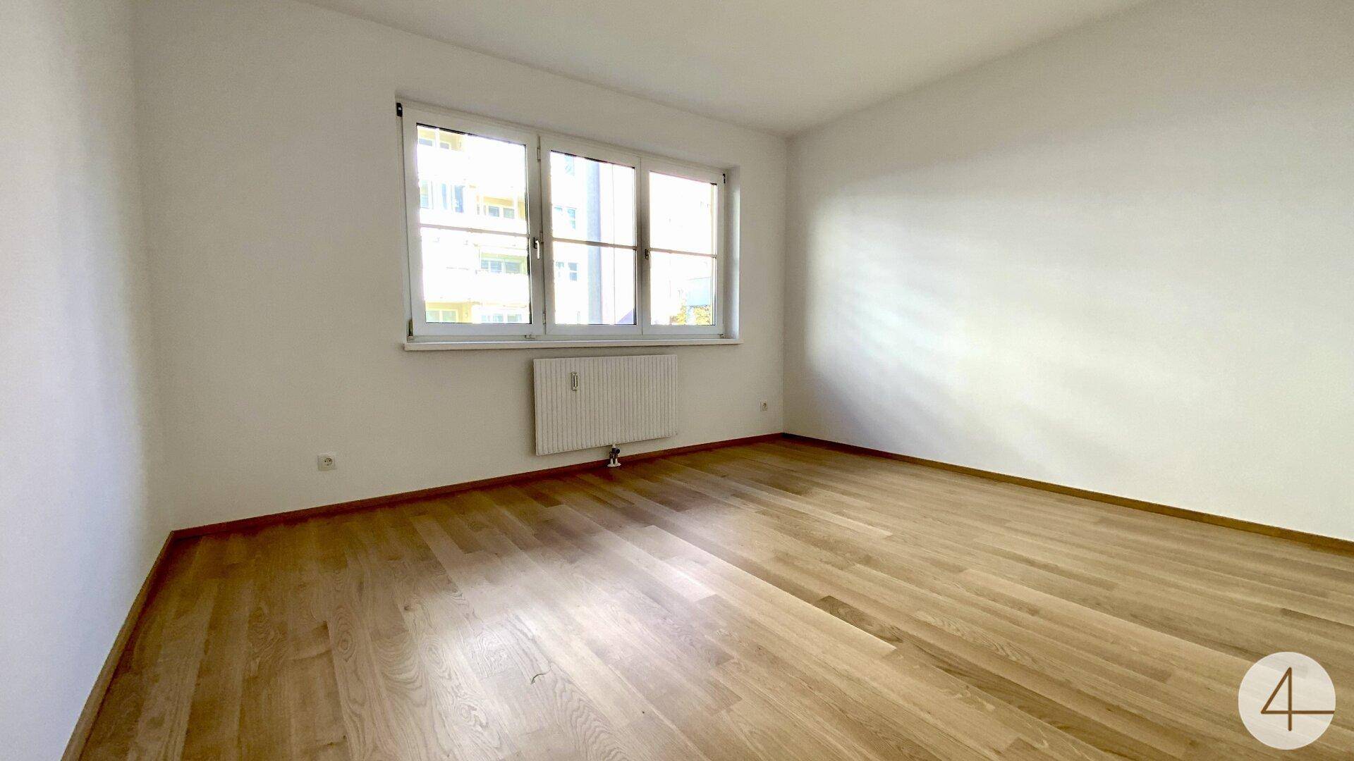 Helles Schlafzimmer mit Eichenparkett, weißen Wänden und großem Fenster.