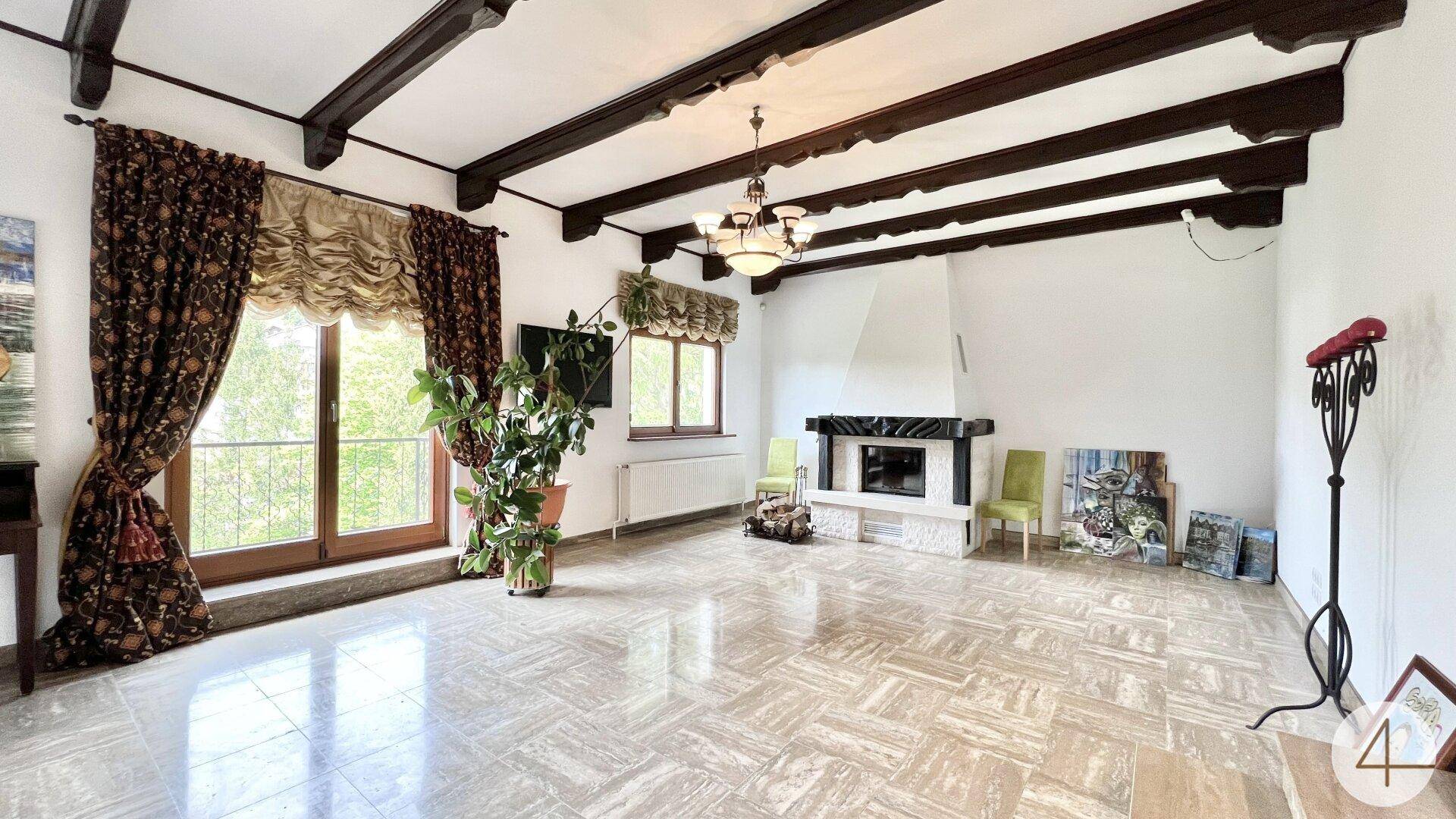 Geräumiges Wohnzimmer mit Holzbalkendecke, Kamin und großen Fenstern zum Balkon.