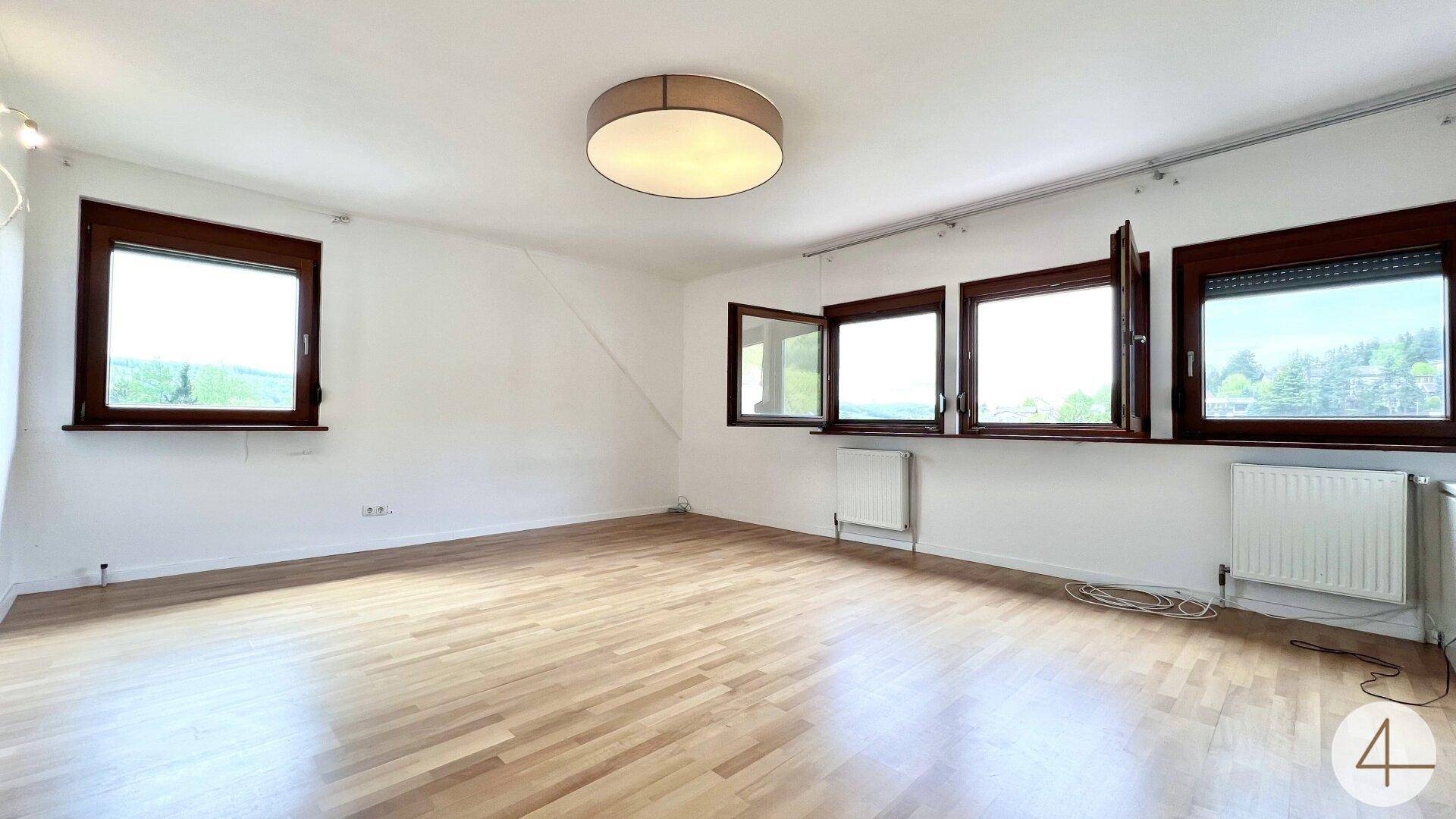 Helles Zimmer mit Holzparkettboden und mehreren Fenstern, die viel Tageslicht hereinlassen.