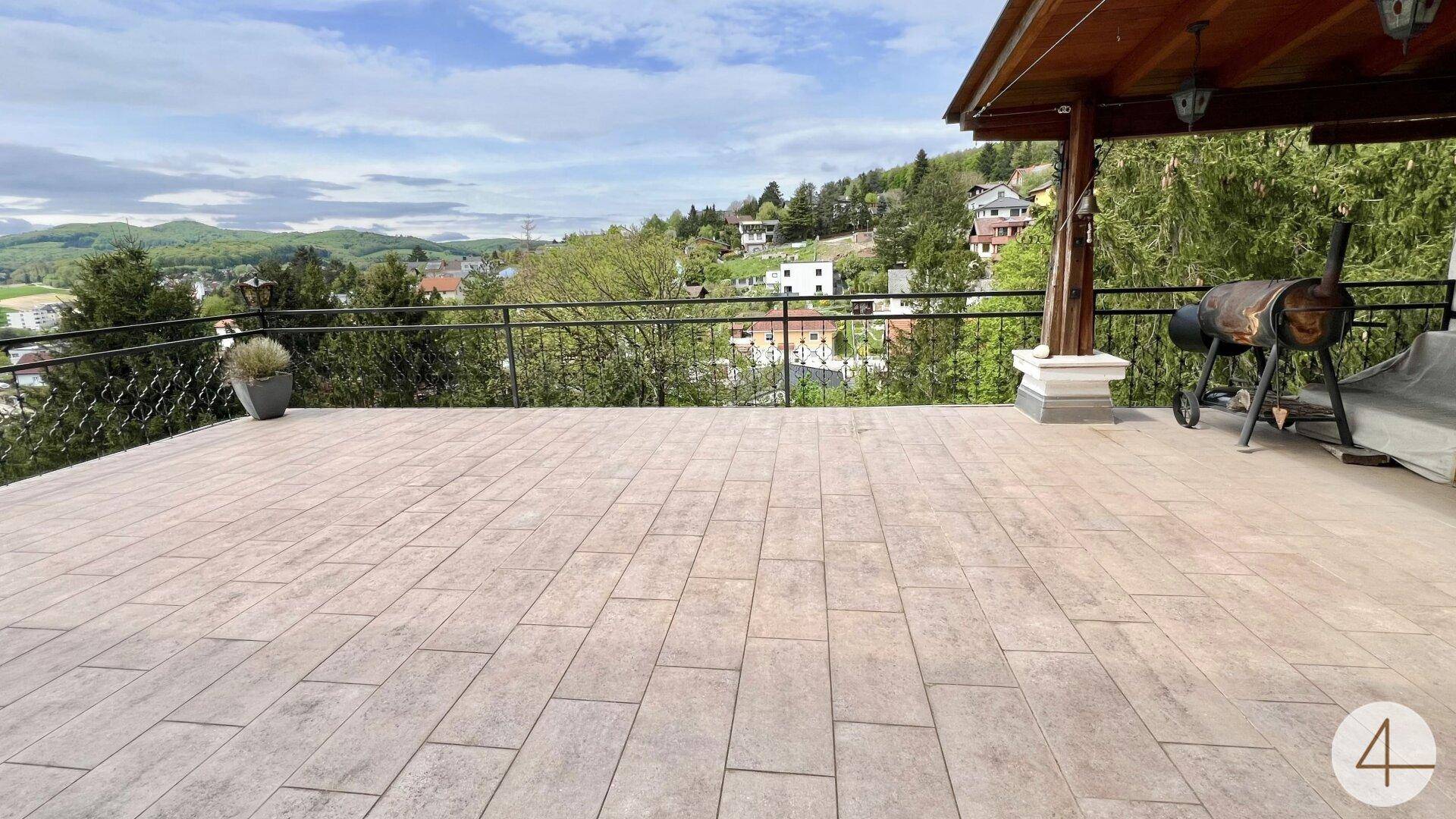 Große gepflasterte Terrasse mit weitem Blick auf die umliegende grüne Landschaft.