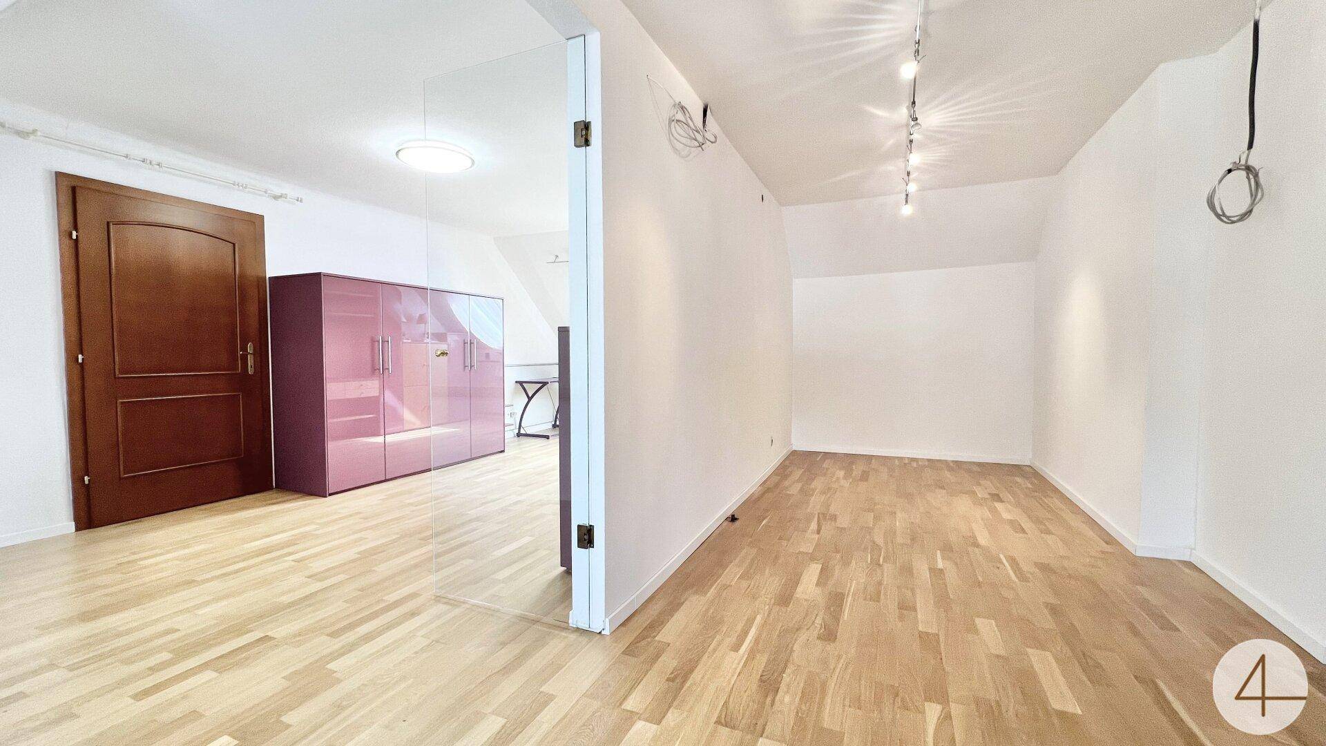 Helles Zimmer mit Holzparkettboden und Zugang zu einem weiteren Bereich.