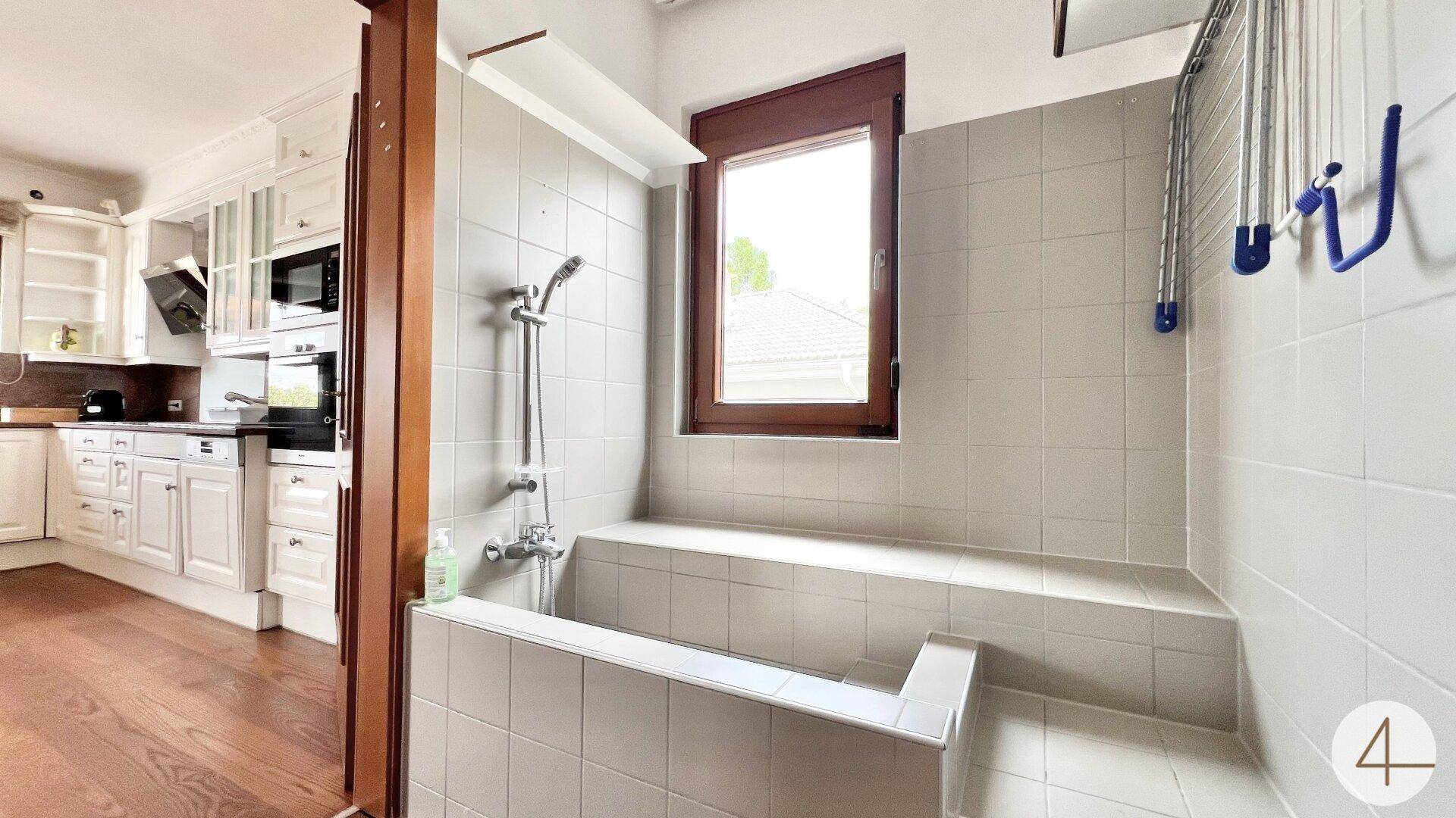 Badezimmer mit integrierter Badewanne, Dusche und Fenster, angrenzend an die Küche.