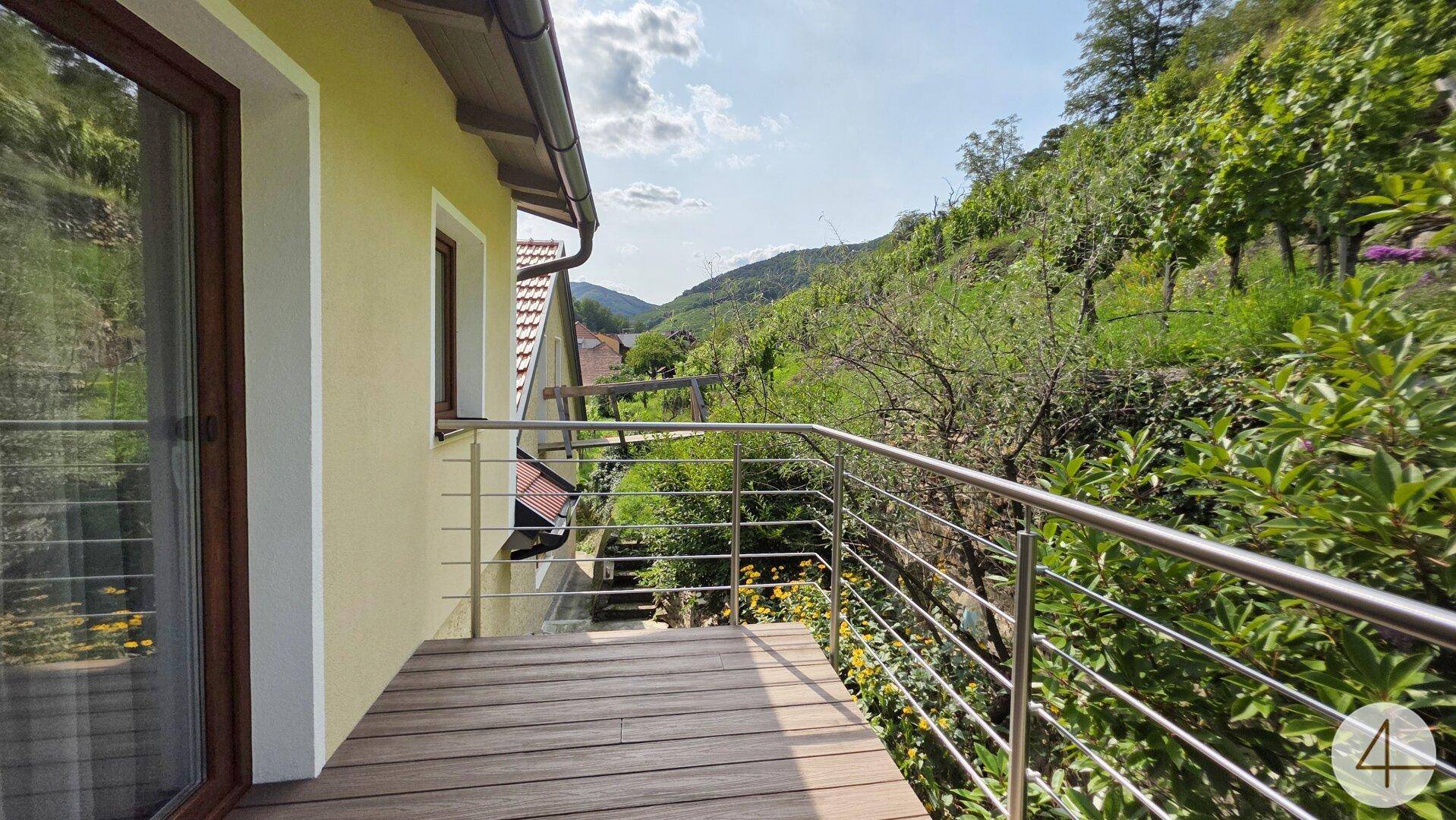 Balkon mit Holzboden und Geländer, der einen malerischen Ausblick auf die umliegenden Weinberge bietet.