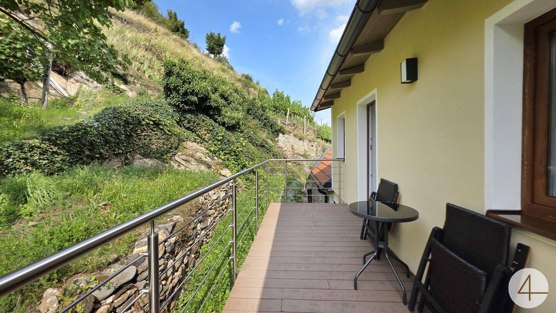 Sonniger Balkon mit Holzboden, Metallgeländer und weitem Blick auf die grünen Weinberge.