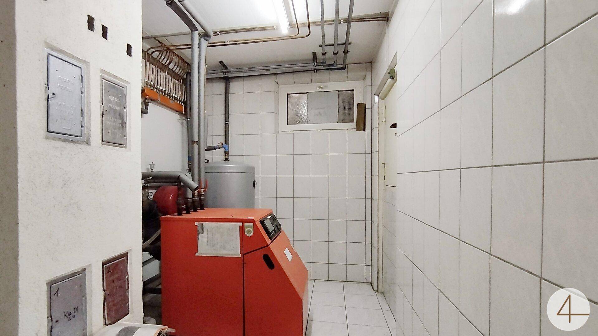 Funktionaler Heizungsraum mit rotem Heizkessel, Warmwasserspeicher und gefliesten Wänden und Boden.