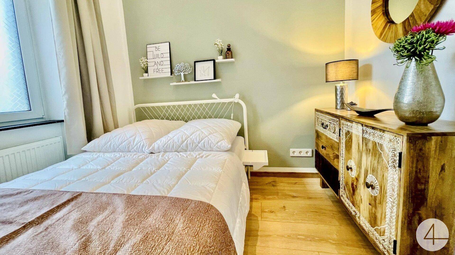 Helles Schlafzimmer mit Doppelbett, Holzboden und einem dekorativen Holzschrank.