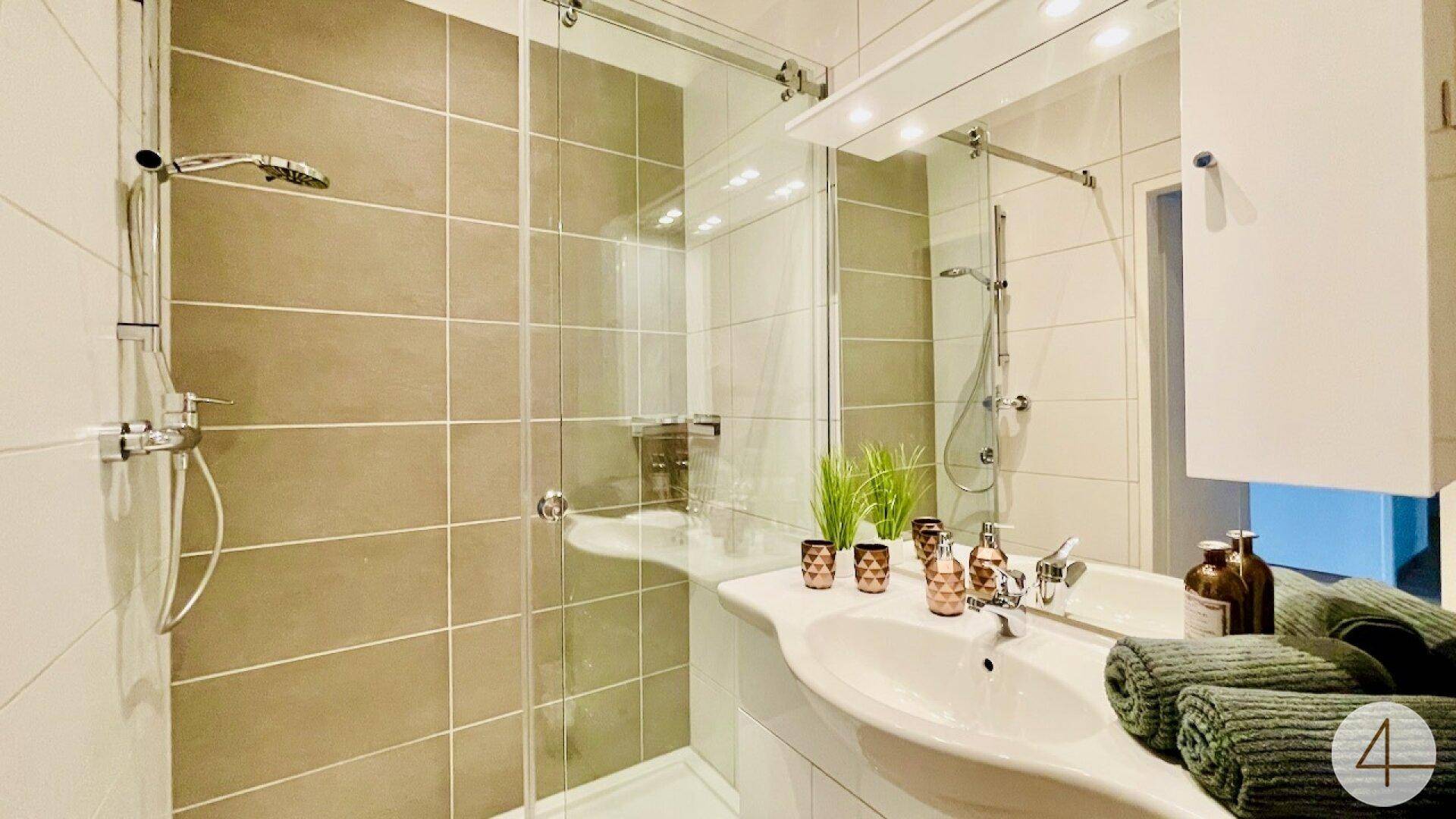 Modernes Badezimmer mit Duschkabine, Einzelwaschbecken und beigen Fliesen.