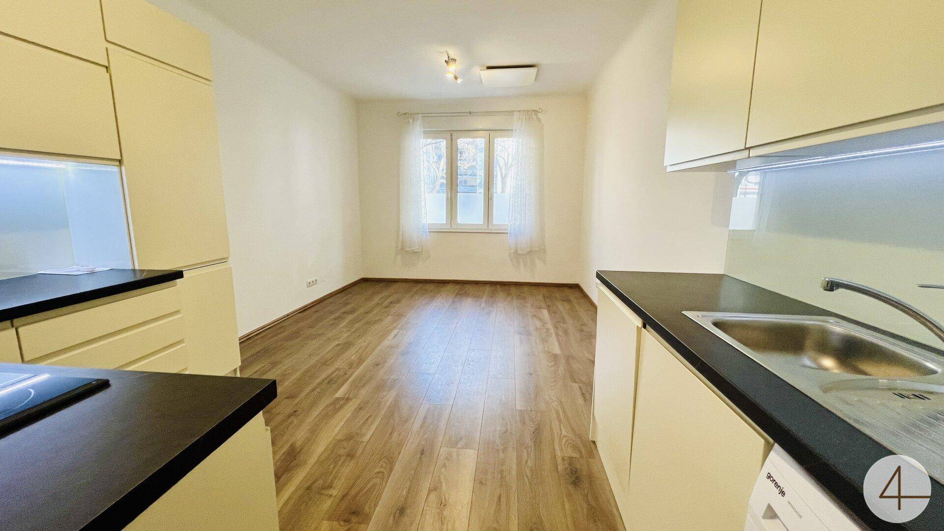 Offener Wohnbereich mit Küchenzeile, Laminatboden und Fenster für natürliches Licht.
