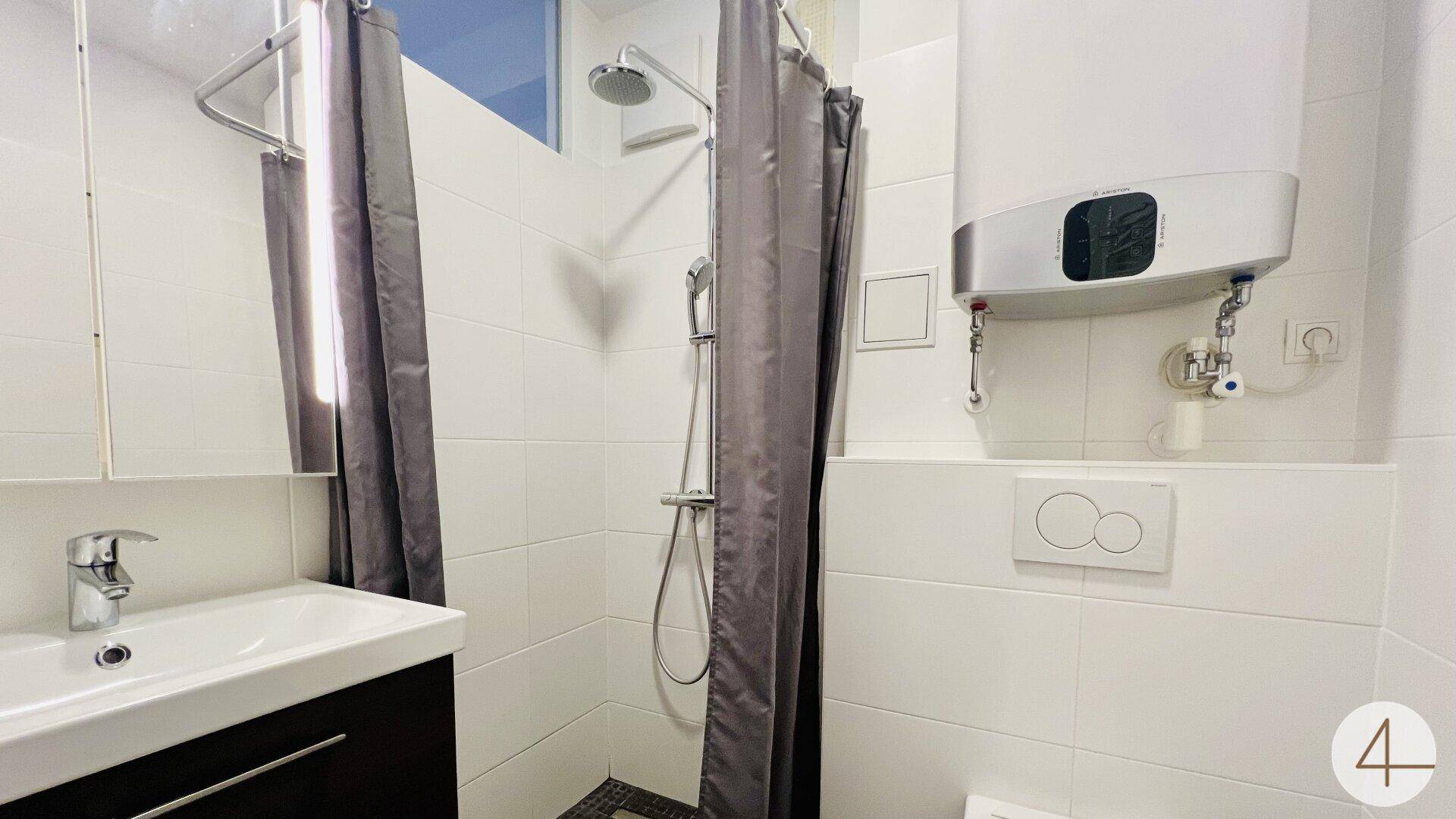 Kleines Badezimmer mit Dusche, Waschbecken und wandhängendem WC in weiß gefliestem Raum.
