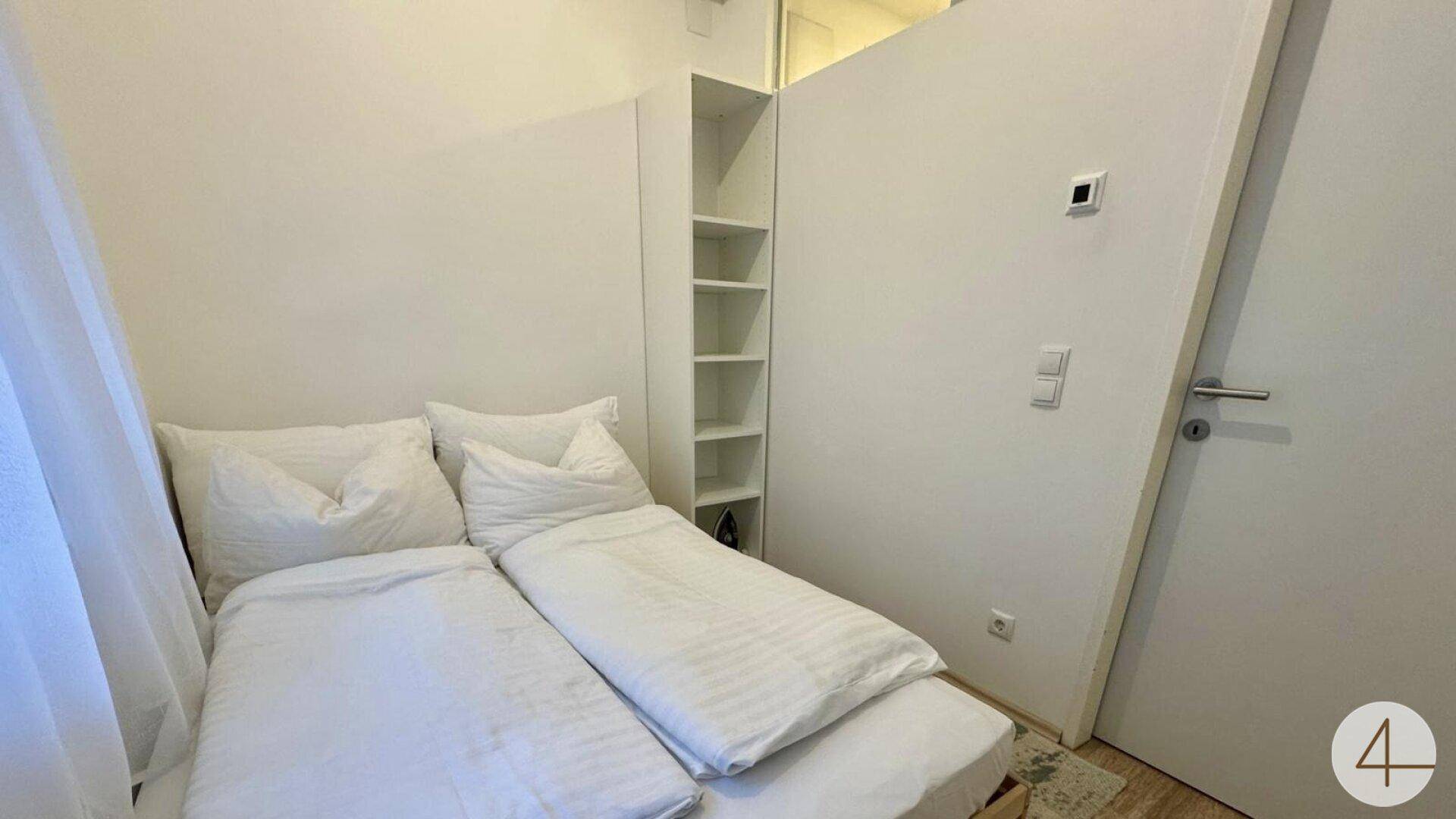 Gemütliches Schlafzimmer mit zwei Einzelbetten, weißen Wänden und integriertem Regal.
