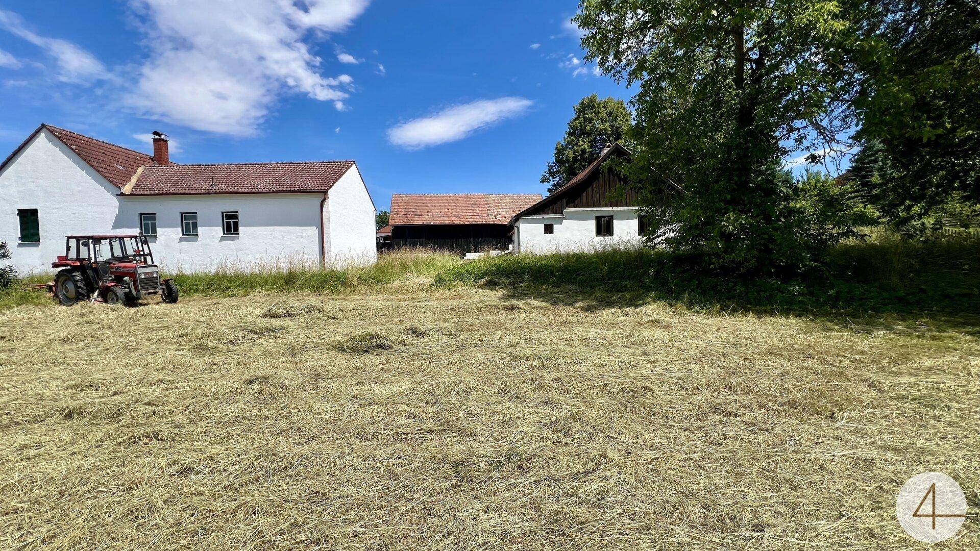 Ländliches Anwesen mit weiten Grasflächen und einem Traktor unter blauem Himmel.