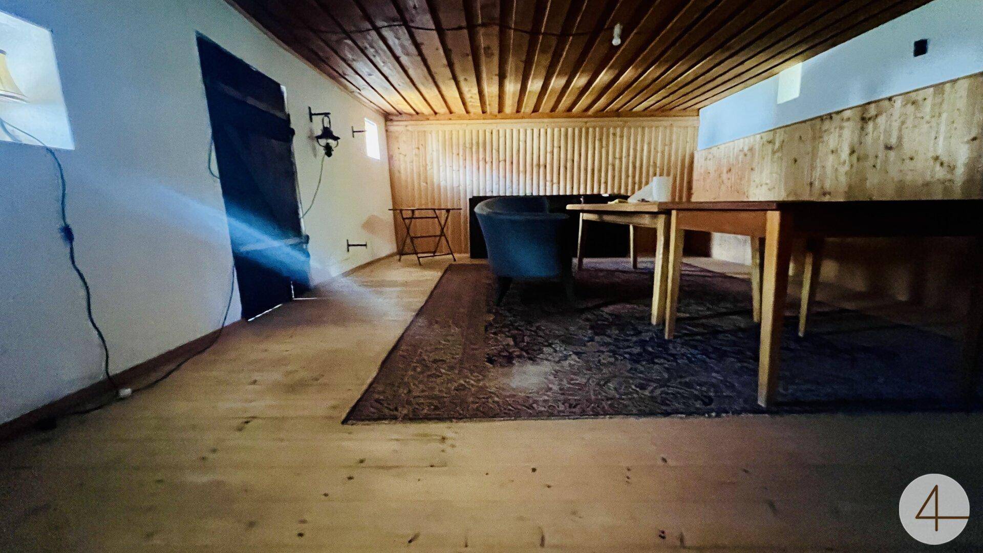 Rustikaler Raum mit Holzboden und Holzdecke, beleuchtet durch eine Wandlampe.