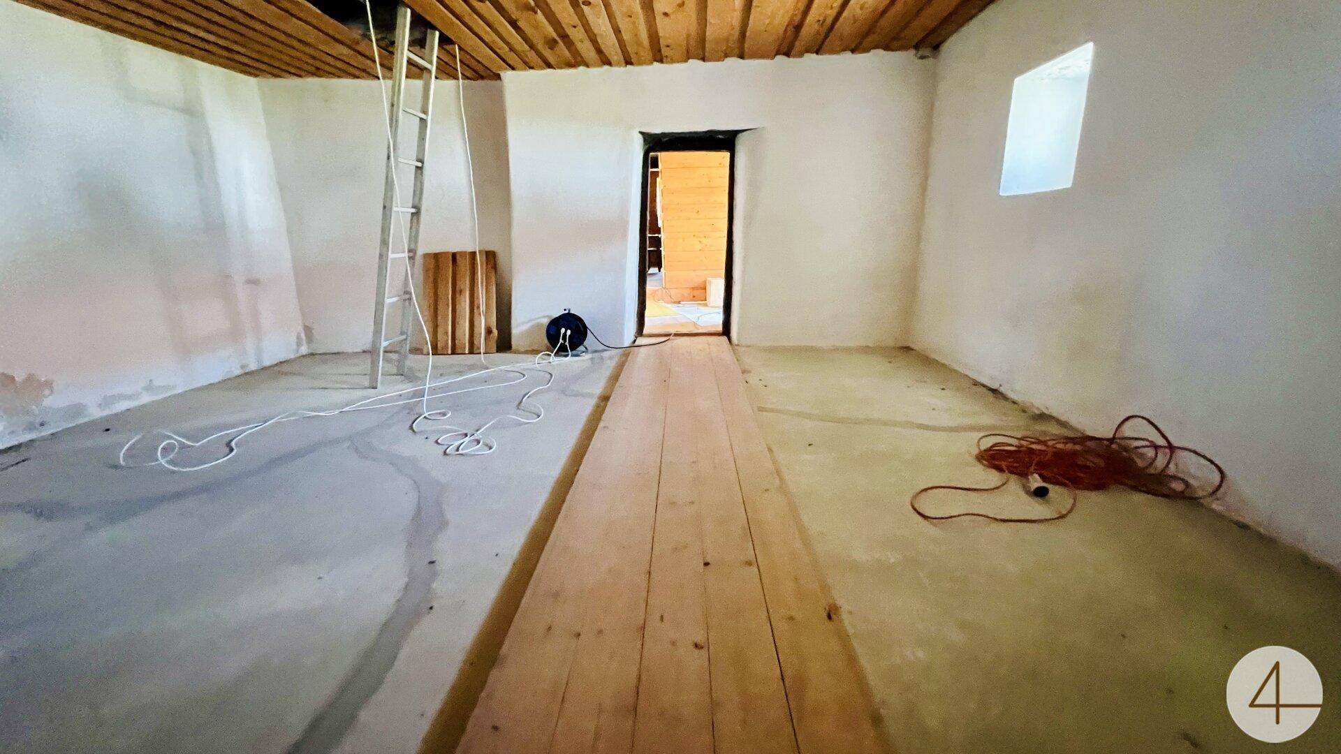Leerer Raum in Renovierung mit Holzboden und weiß gestrichenen Wänden.