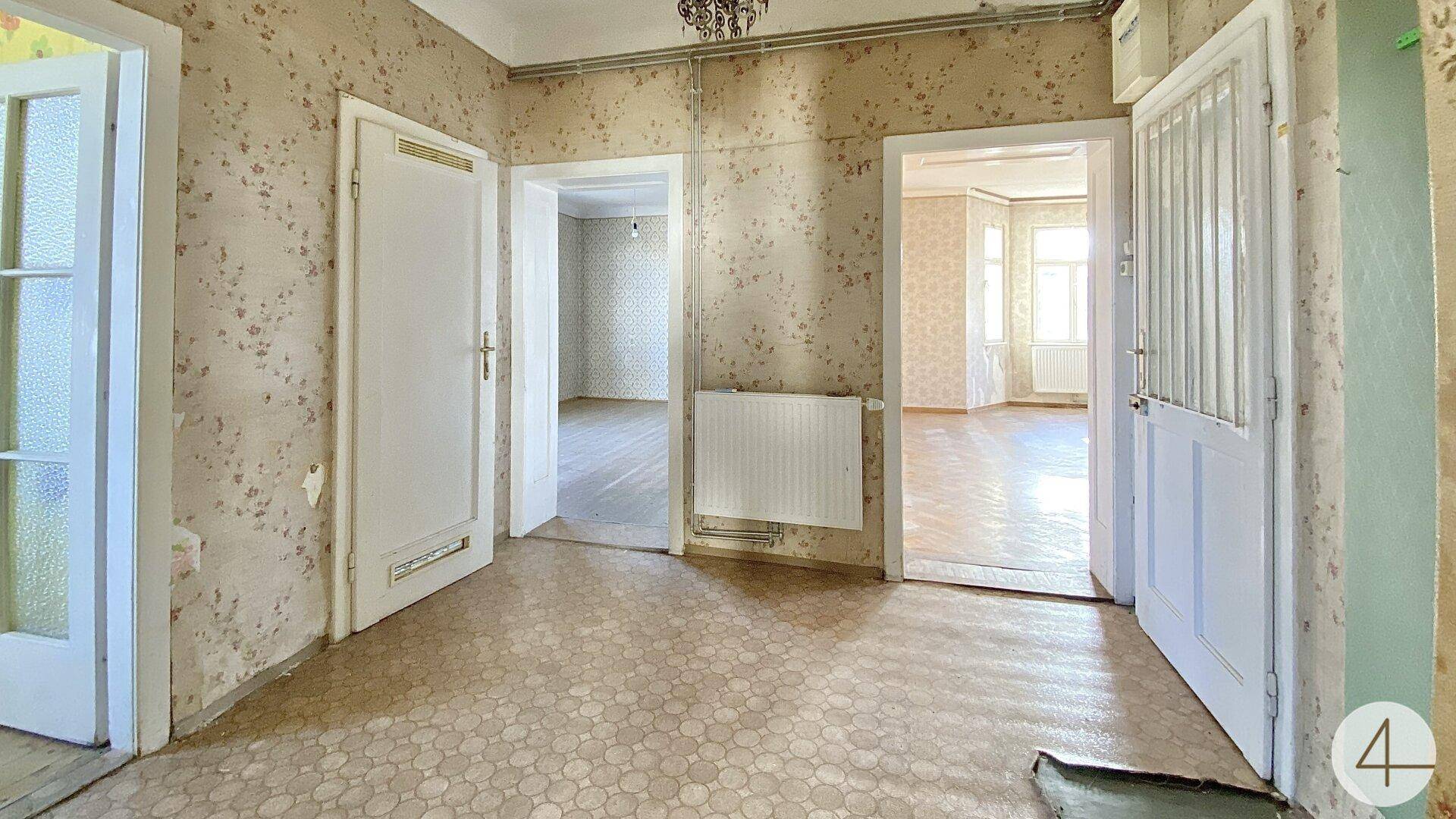 Flur mit gemusterter Tapete, Linoleumboden und mehreren Türen zu angrenzenden Räumen.